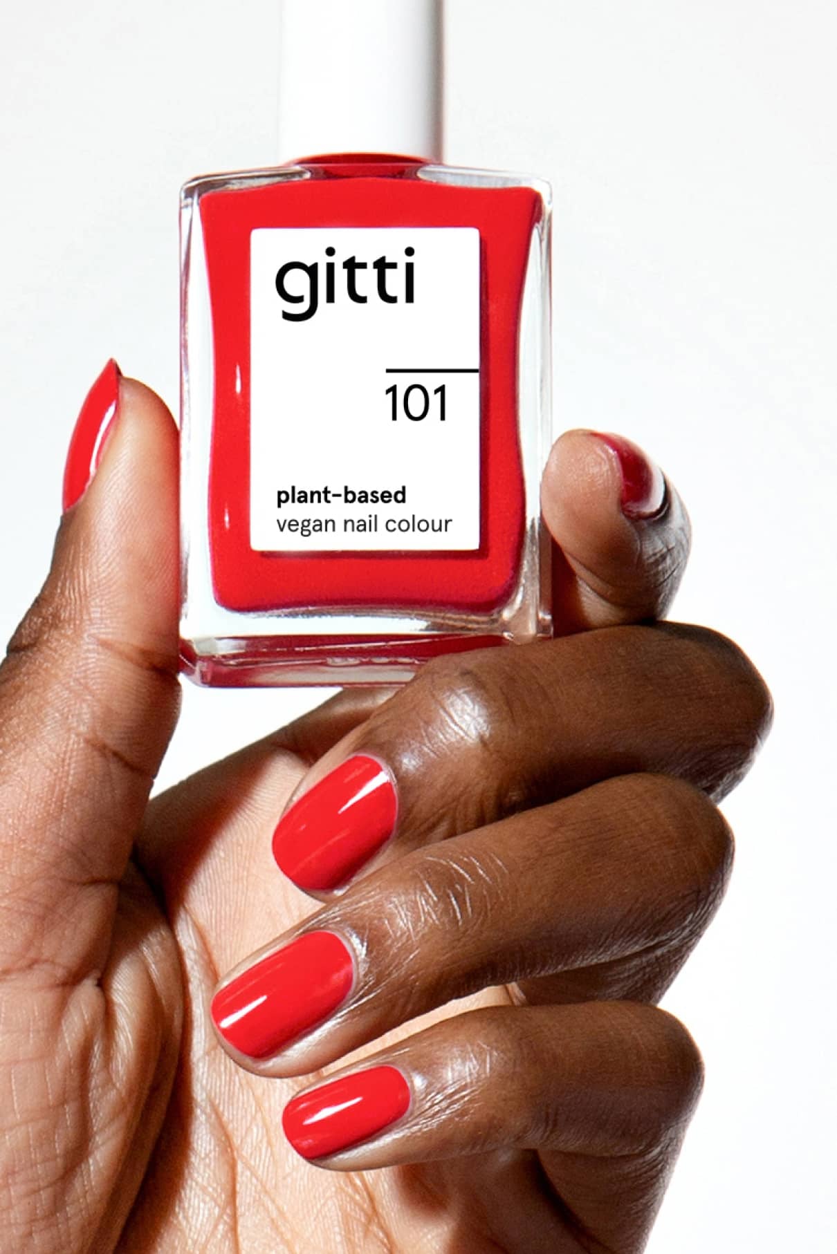 Eine Hand mit rot lackierten Nägeln hält eine Flasche gitti no. 101 pflanzliche, vegane Nagelfarbe in feurigem Rot, passend zu dem leuchtenden Lack auf den Fingernägeln.