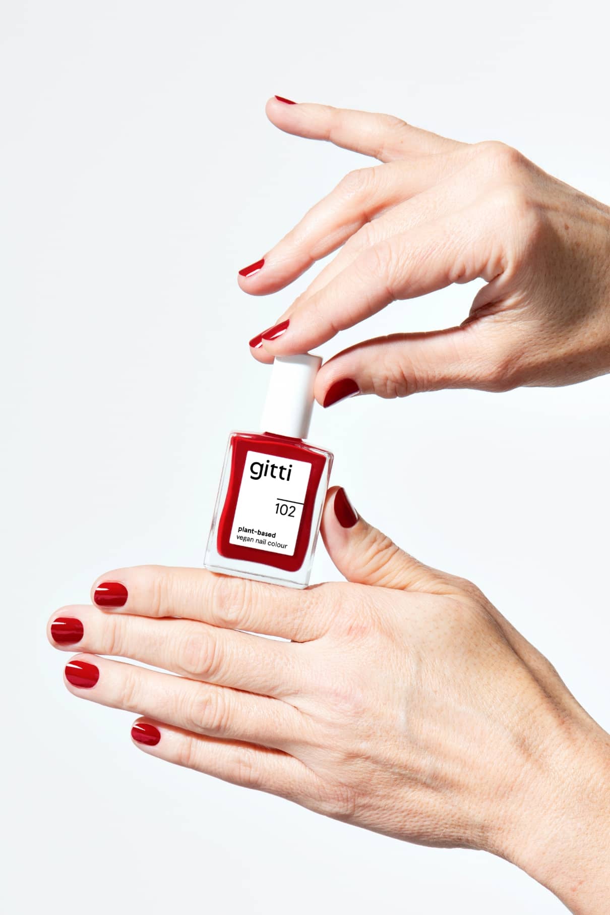 Eine Person mit rot lackierten Nägeln hält eine Flasche gitti no. 102 Nagellack vor einem weißen Hintergrund.