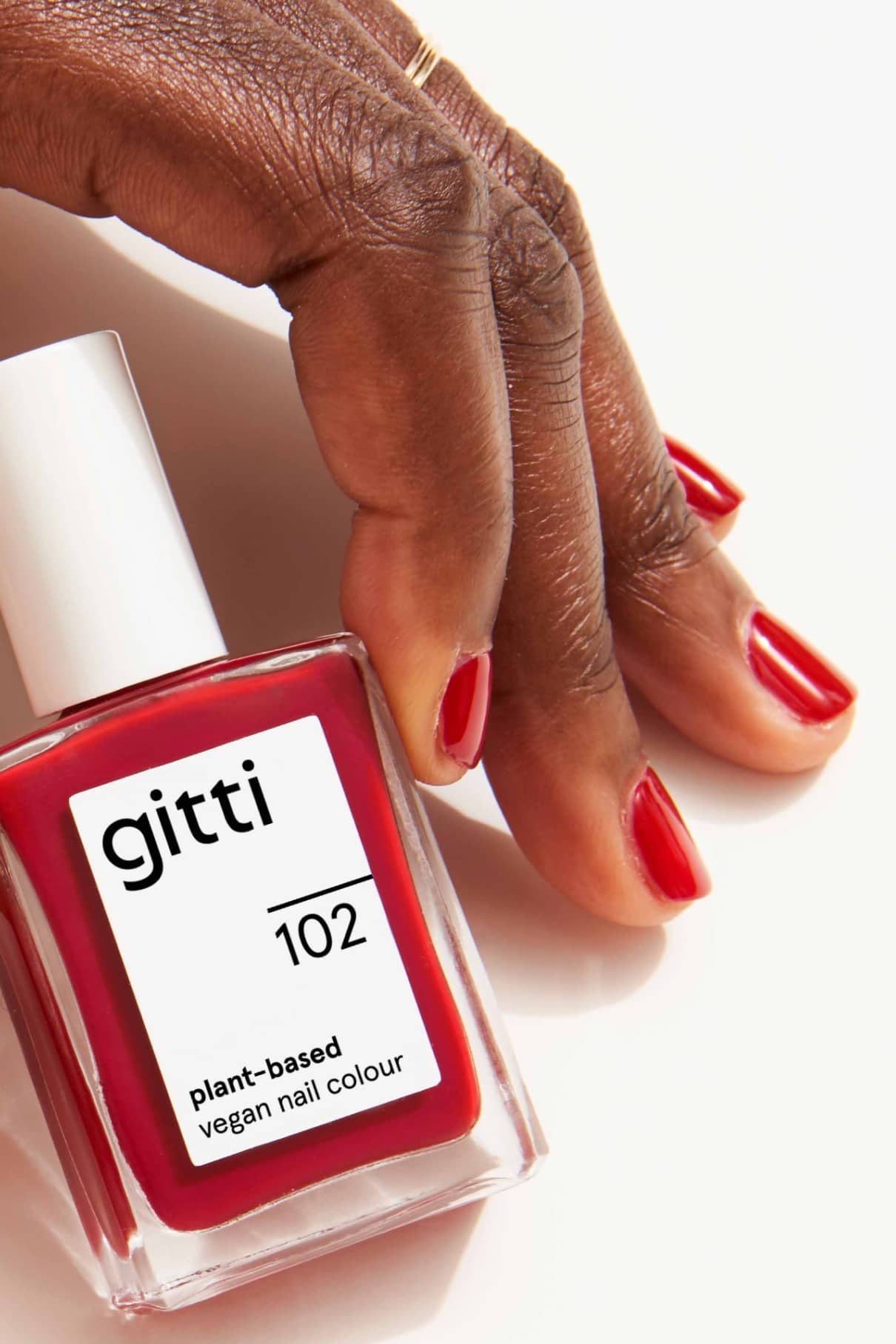 Eine Hand mit rot lackierten Nägeln wie Rotwein ruht neben einer Flasche gitti no. 102, einem veganen Nagellack auf pflanzlicher Basis in einem passenden Farbton.