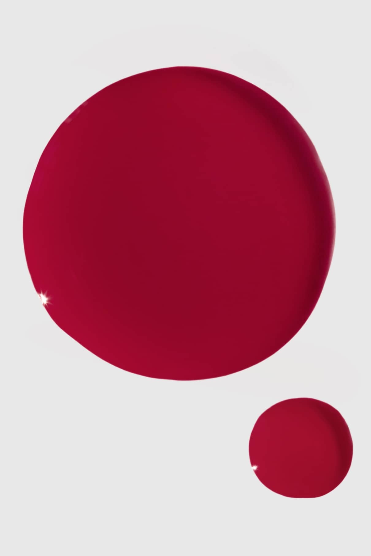 Zwei rote kreisförmige Flüssigkeitstropfen, ein großer und ein kleiner, erinnern an gitti Nr. 102, die sich vor einem schlichten weißen Hintergrund abzeichnen, wobei auf jedem Tropfen Lichtreflexe zu sehen sind.