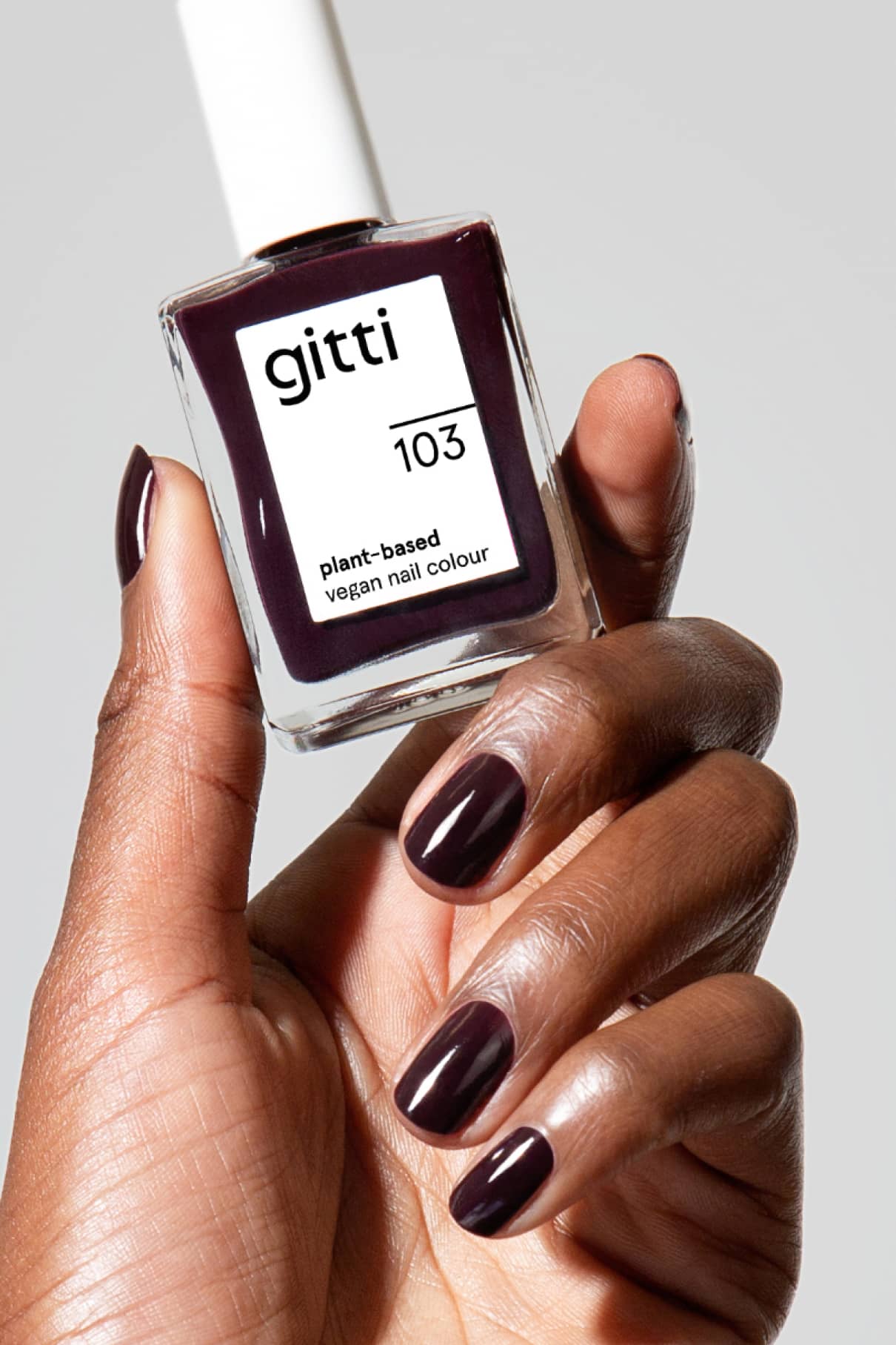 Eine Hand mit dunkel lackierten Nägeln hält eine Flasche Colour Up Duo und hebt die leuchtende, vegane Formel hervor.