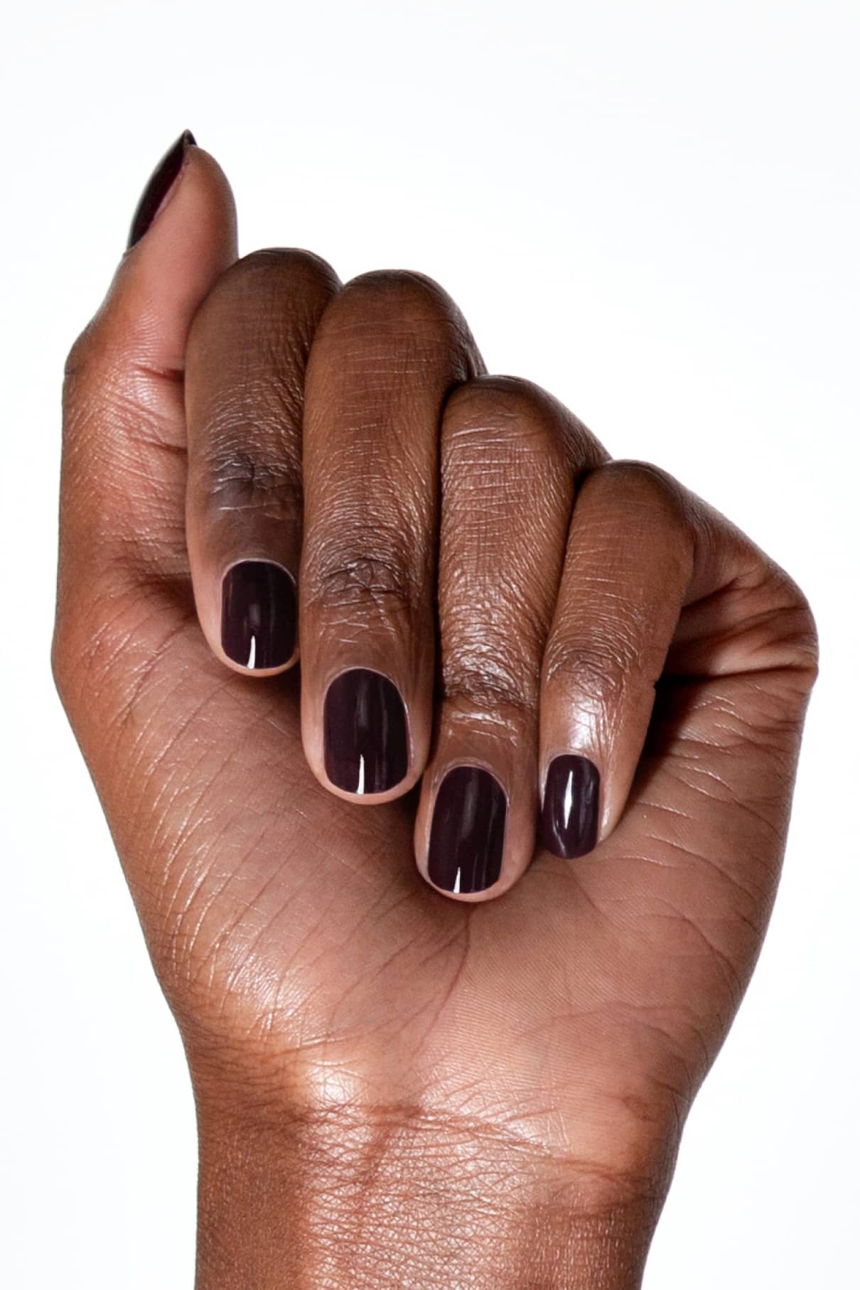 Eine Hand mit dunkler Haut und kurzen, sorgfältig manikürten Nägeln, die in dem glänzenden, dunkelbraunen Aubergine-Ton von gitti no. 103 lackiert sind, ist mit nach innen gerollten Fingern abgebildet.