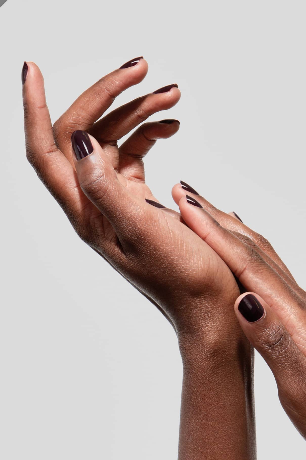 Zwei Hände mit gitti no. 103 Nagellack, einem tiefen Aubergine-Ton, sind anmutig vor einem schlichten hellgrauen Hintergrund posiert.
