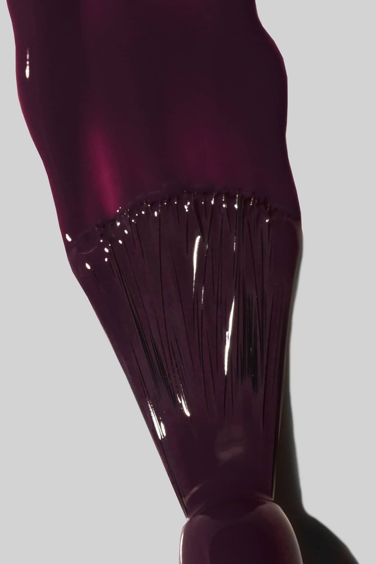 Nahaufnahme eines Nagellackpinsels, mit dem gitti no. 103, ein intensiver auberginefarbener Farbton, auf eine glatte hellgraue Oberfläche.