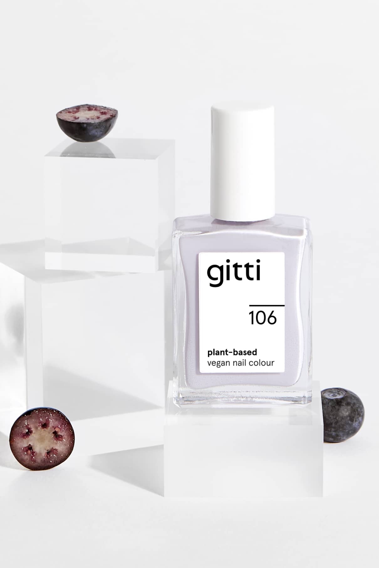 Eine Flasche gitti no. 106 pflanzliche vegane Nagelfarbe in Pastellblau steht auf klaren Blöcken, umgeben von halbierten Blaubeeren.
