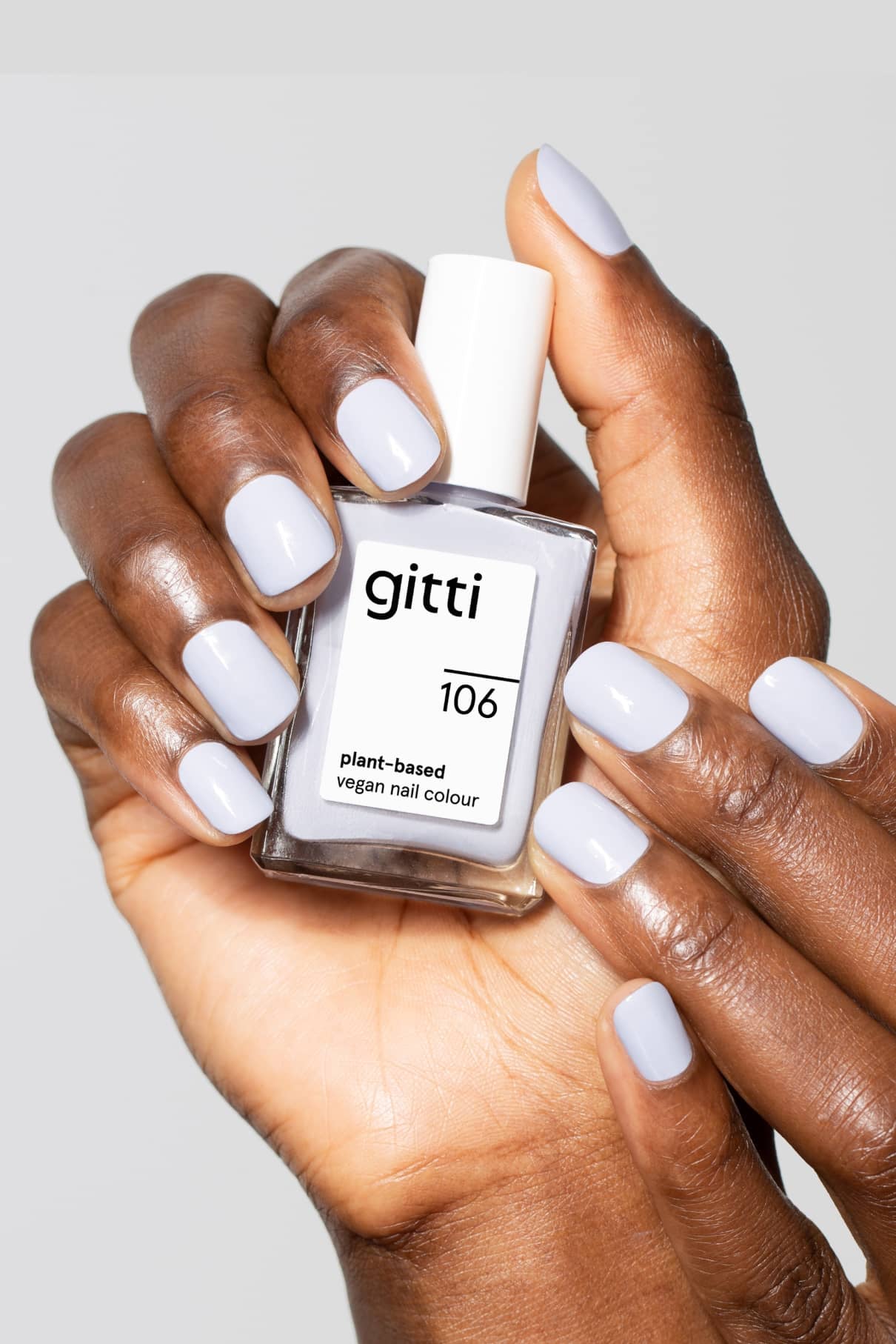 Eine Hand hält eine Flasche mit gitti no. 106, einem veganen Nagellack auf Pflanzenbasis. Die Nägel sind in einem Pastellblau lackiert, das sanft zwischen Puderblau und Hellblau schimmert.