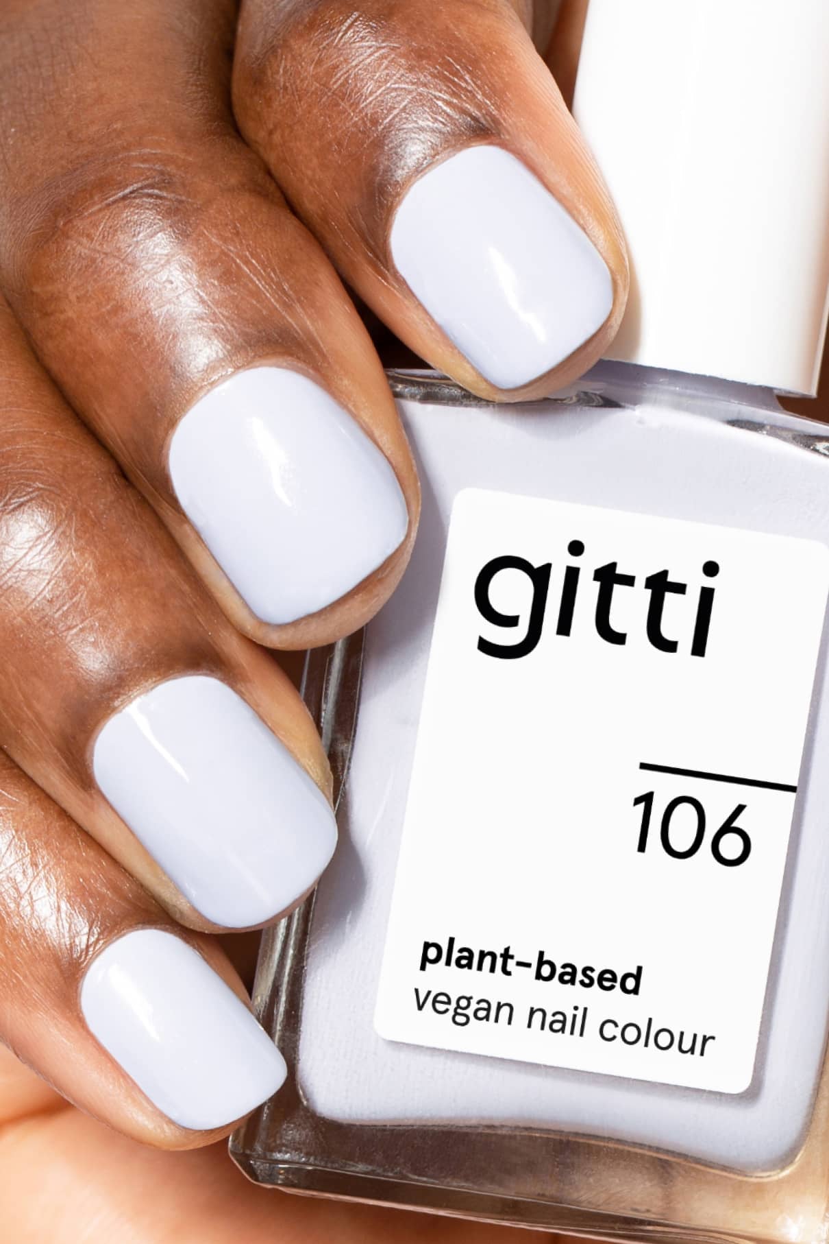 Eine Hand mit kurzen, sauber manikürten, hellblau lackierten Nägeln hält eine Flasche mit der Aufschrift gitti no. 106 vegane Nagelfarbe auf Pflanzenbasis.