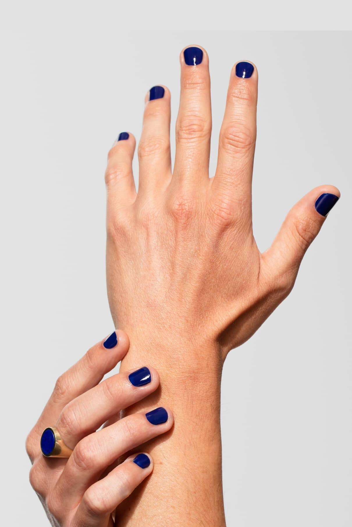Zwei Hände mit kurzen Nägeln in intensivem Blau lackiert - Gitti Nr. 108. Eine Hand hält sanft das Handgelenk der anderen, in dem ein goldener Ring zu sehen ist. Der kräftige Farbton Mitternachtsblau hebt sich von einem neutralen Hintergrund ab.
