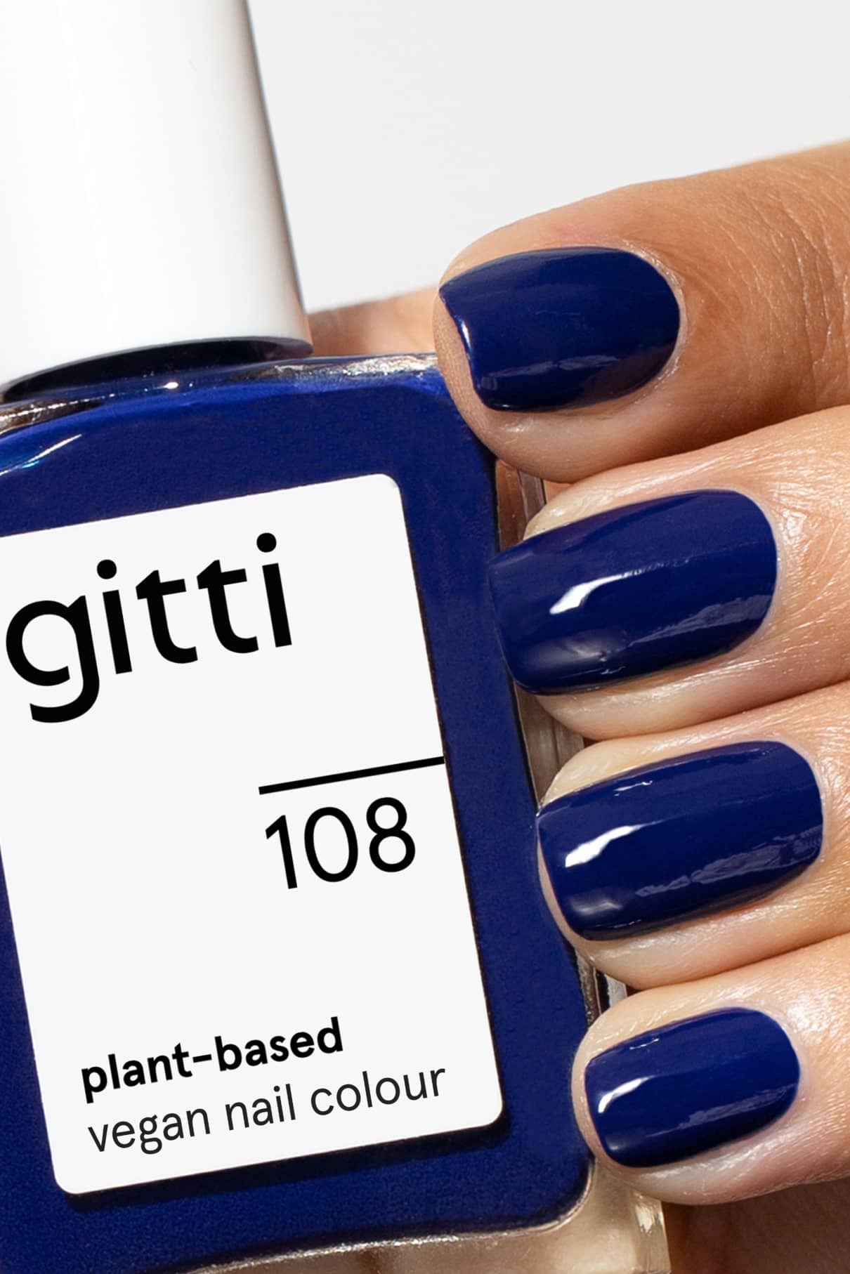 Eine Hand mit kurzen, intensiv blau lackierten Nägeln hält eine quadratische Flasche mit gitti no. 108, einem veganen Nagellack auf pflanzlicher Basis im gleichen nachtblauen Farbton.