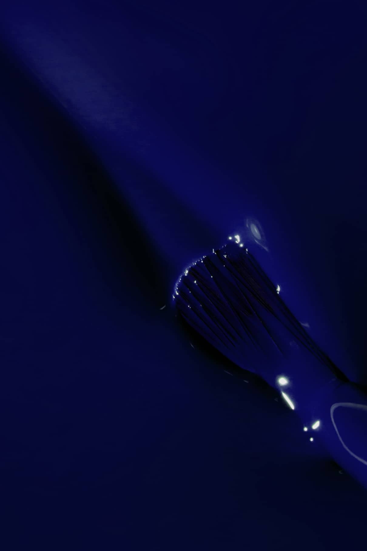 Ein Pinsel trägt gitti no. 108 auf eine glatte Oberfläche, wobei Lichtreflexe das intensive Blau der glänzenden Farbe verstärken.