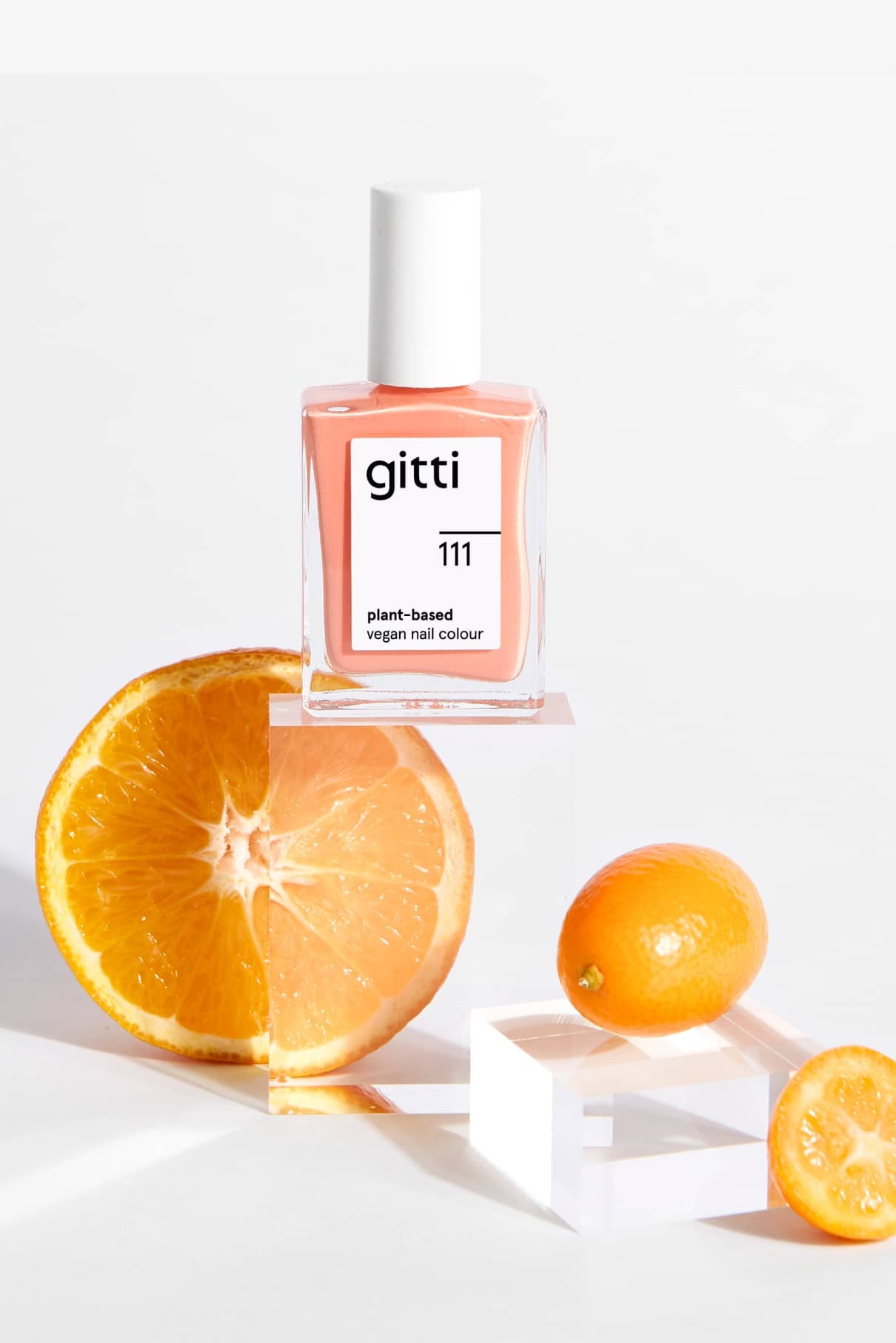 Eine Flasche Gitti Nr. 111 steht auf einem durchsichtigen Block neben einer halbierten Orange und einer ganzen Kumquat vor einem weißen Hintergrund.