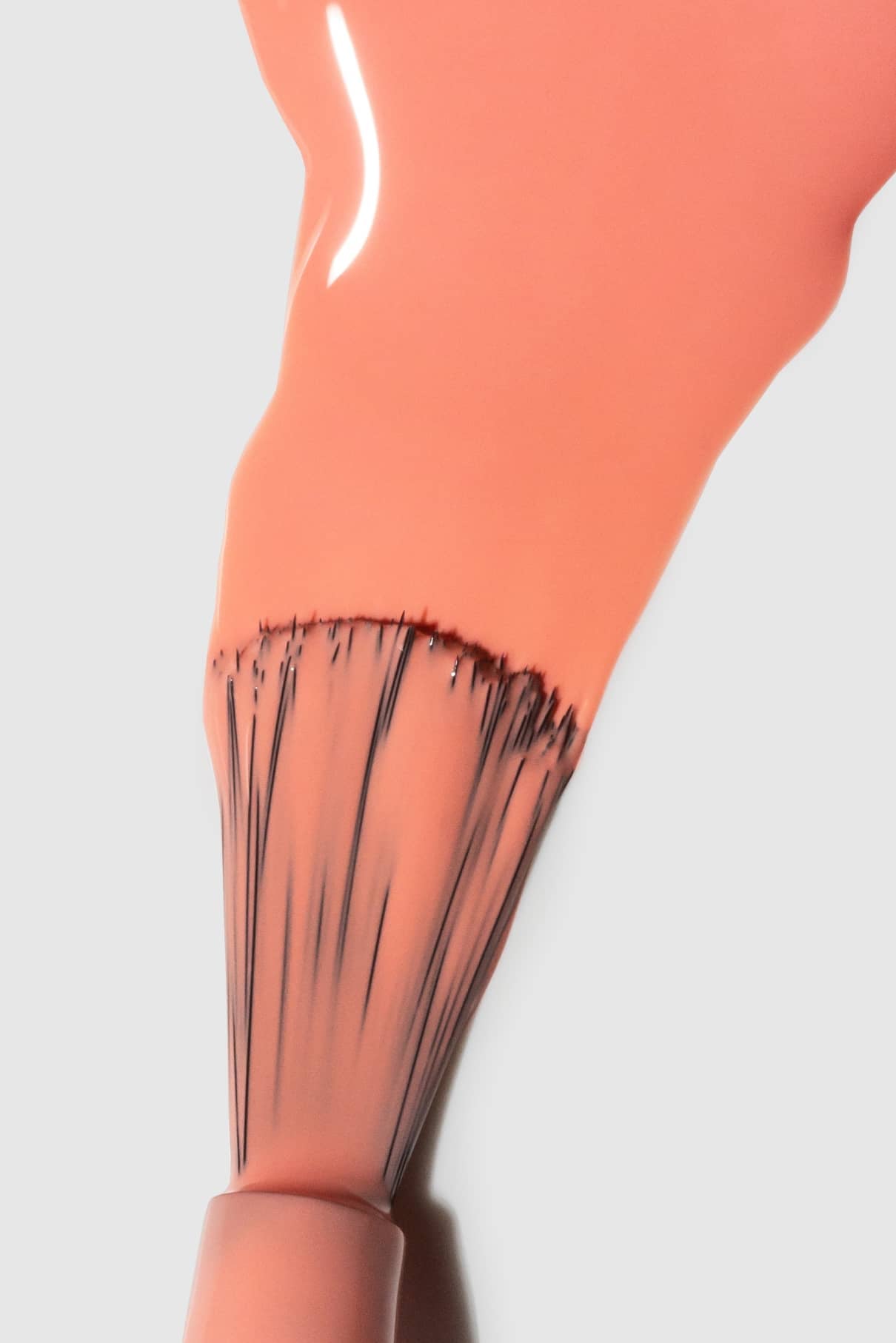 Nahaufnahme eines Nagellackpinsels mit gitti no. 111, ein zartes Pfirsichrosa mit warmen Untertönen, der auf eine weiße Fläche aufgetragen wird.