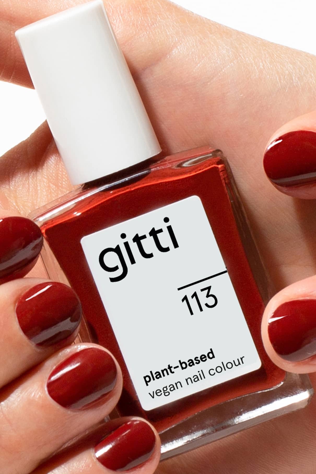 Eine Hand hält eine Flasche gitti no. 113. Die Nägel sind im passenden tiefroten, braun-roten Farbton dieses pflanzlichen, veganen Nagellacks lackiert.
