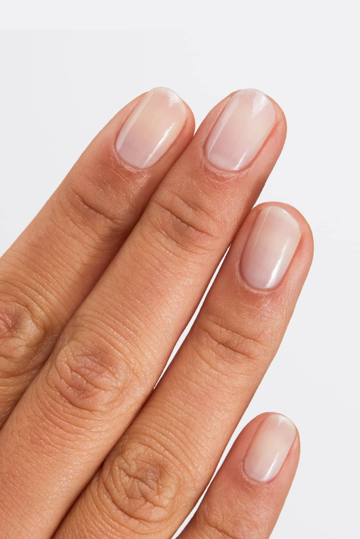 Nahaufnahme einer Hand mit drei sichtbaren Fingern und sauberen, kurzen Naturnägeln, die mit Gitti Nr. 114, einem halbtransparenten Blassrosa Nagellack, vor einem hellen Hintergrund.