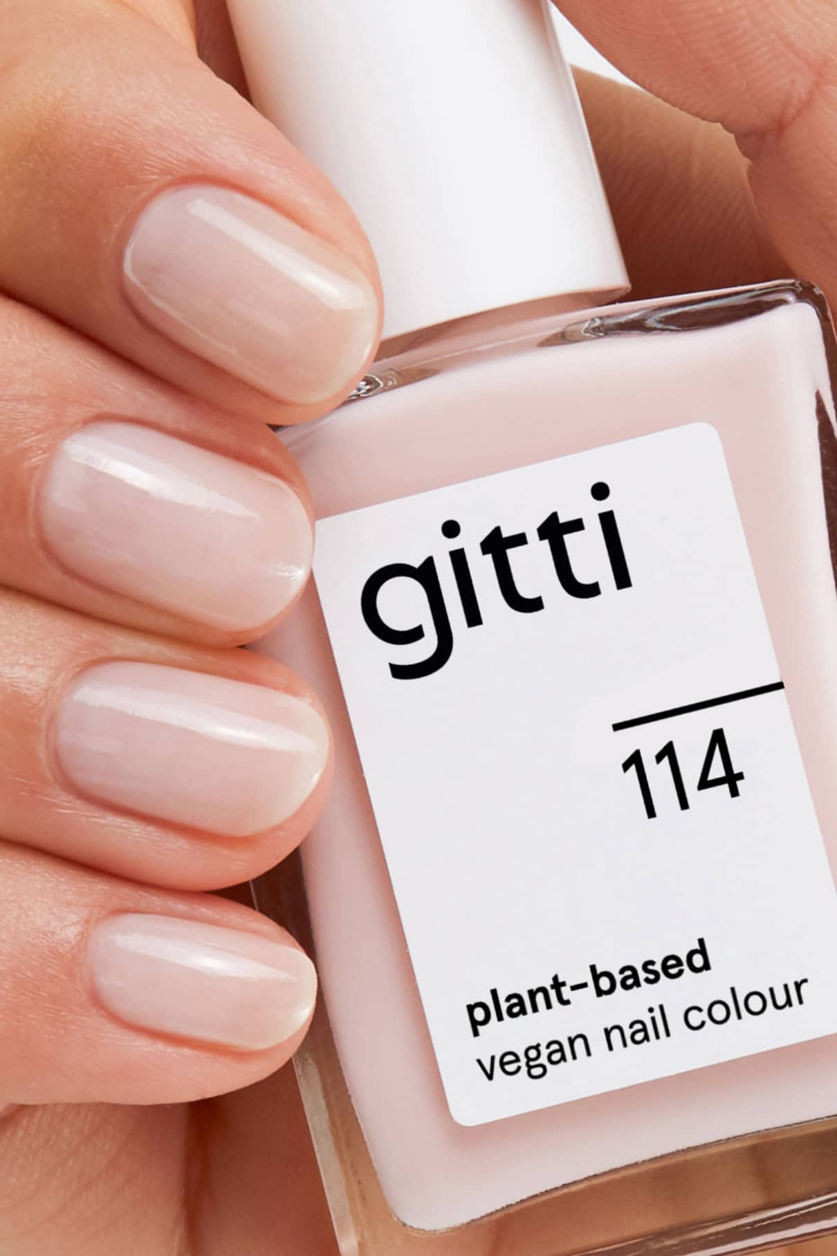 Eine Hand mit sauber manikürten Nägeln hält eine Flasche aus dem Perfect Finish Set mit der pflanzlichen, veganen Nagelfarbe gitti 114 in Blassrosa, die mit dem High Gloss Top Coat für zusätzlichen Glanz versehen ist.