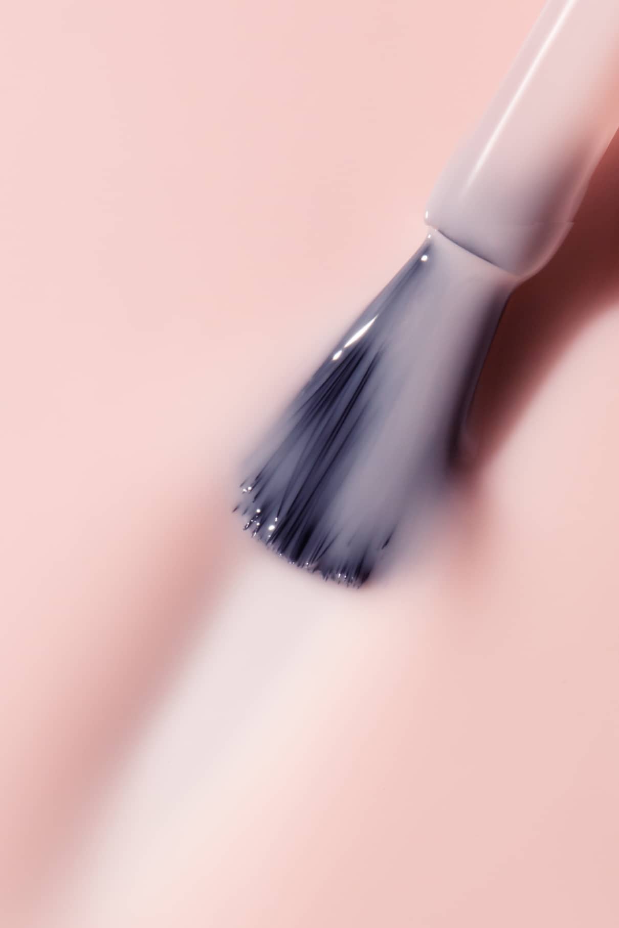 Eine Nahaufnahme eines gitti no. 114 Pinsel beim Auftragen der halbtransparenten Blassrosa-Politur auf eine passende rosa Oberfläche.