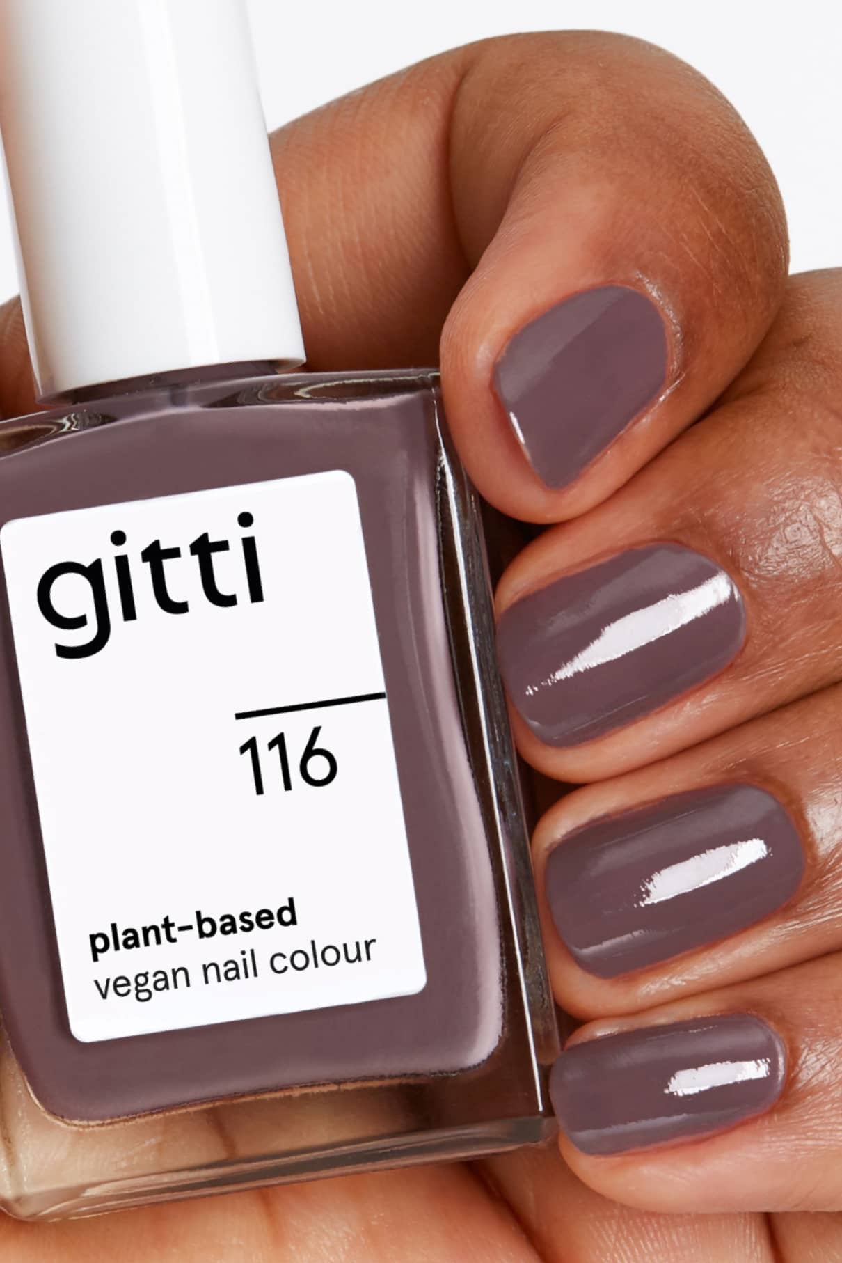 Eine Hand mit kurzen Nägeln, die in einem kühlen Braun mit violettem Unterton lackiert sind, hält eine Flasche mit gitti no. 116, einer veganen Nagelfarbe auf Pflanzenbasis.