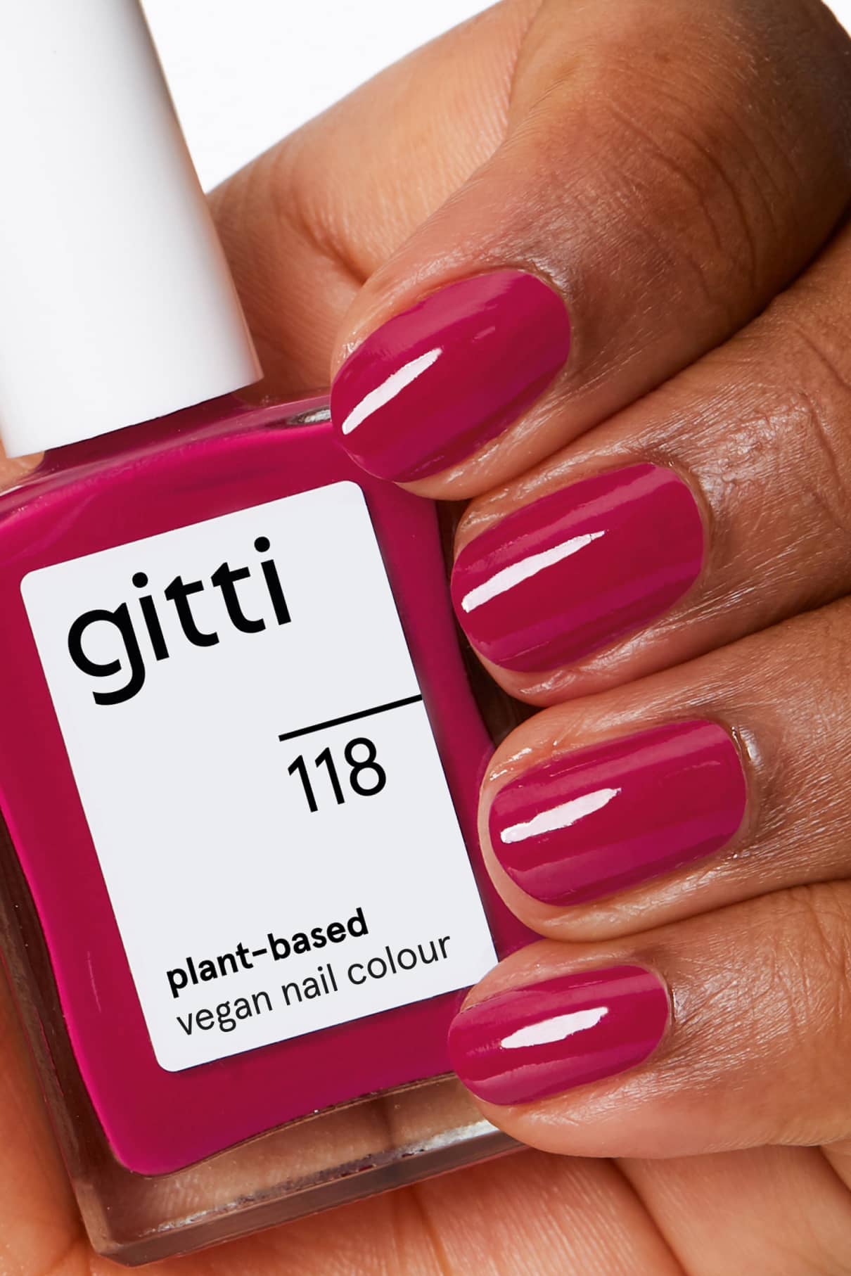 Eine Hand mit kurzen, glänzenden, mit Himbeerot lackierten Nägeln hält eine Flasche gitti no. 118 pflanzlicher, veganer Nagellack in einem passenden Farbton.