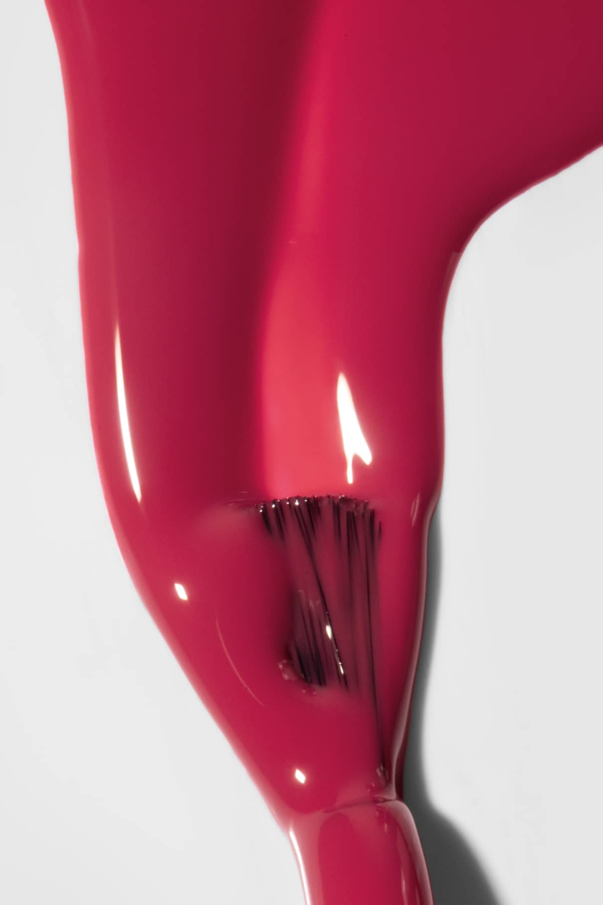 Nahaufnahme eines Pinsels, mit dem glänzender gitti no. 118 Nagellack in Himbeerot auf einer weißen Fläche, mit sichtbaren Pinselstrichen und Lichtreflexion.