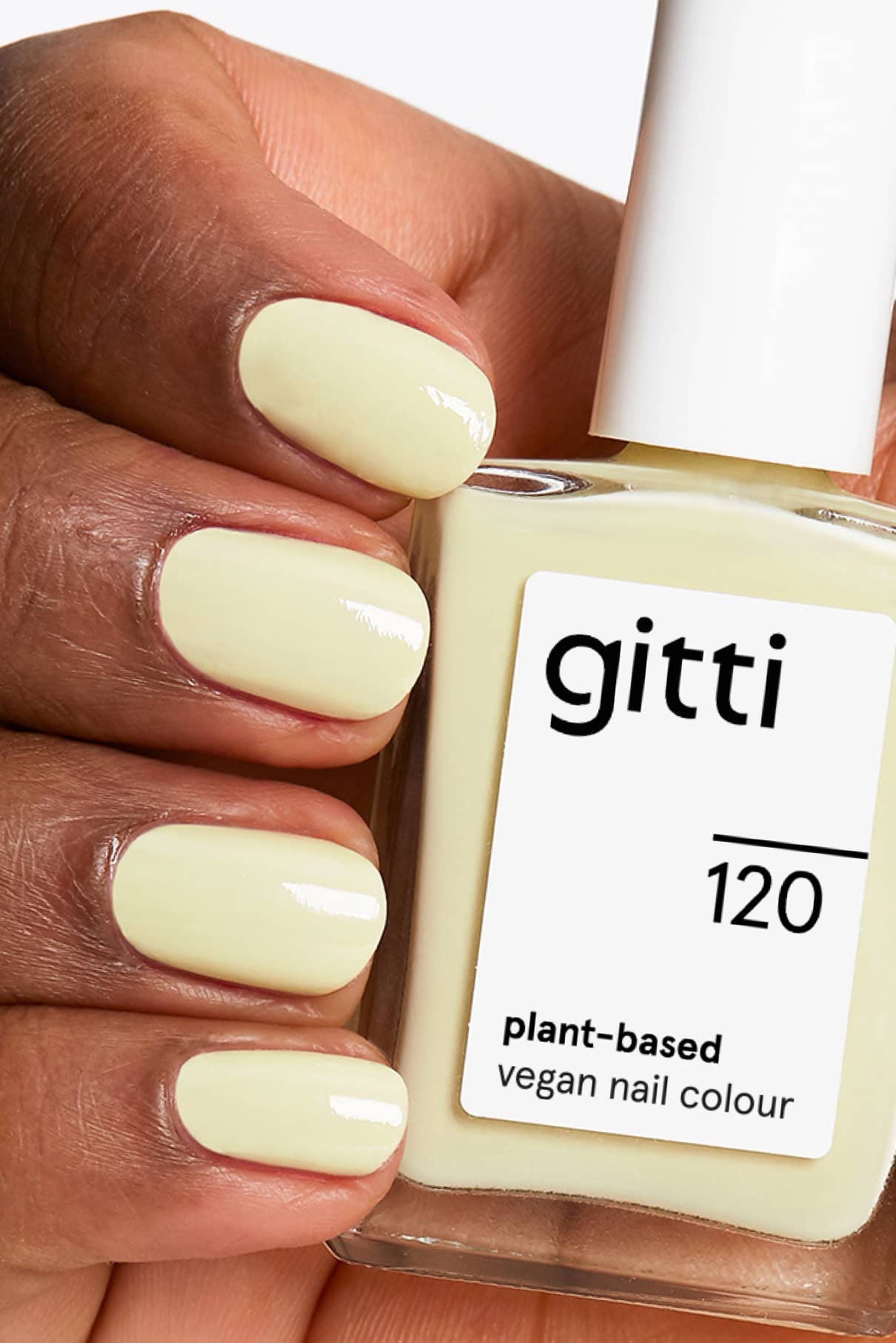 Eine Hand mit blassgelb lackierten Nägeln hält eine Flasche gitti no. 120, einer pflanzlichen, veganen Nagelfarbe in einem pastellfarbenen Zitronenton.