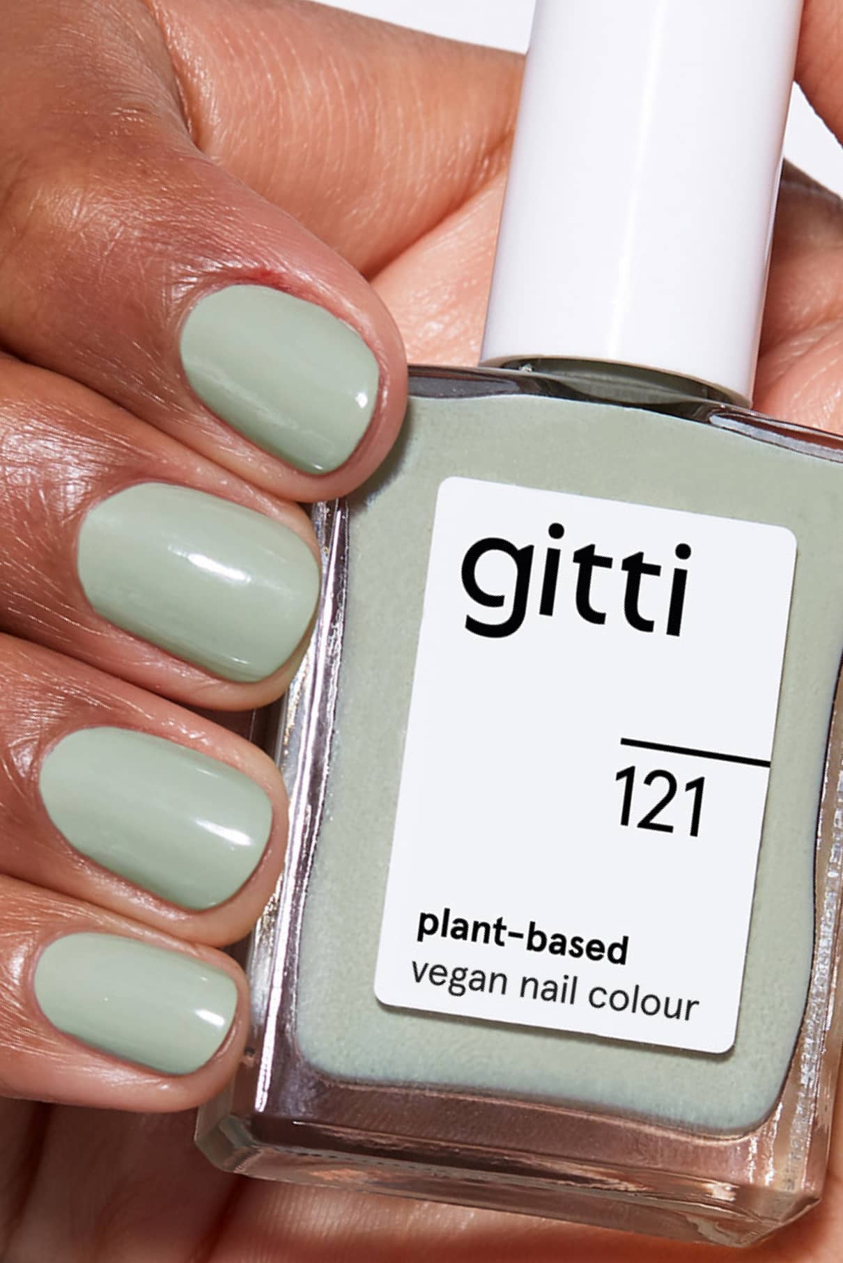 Eine Hand mit hellgrün lackierten Nägeln hält ein Fläschchen von gitti no. 121 - eine pflanzliche, vegane Nagelfarbe in Salbeigrün, ideal für Fans von dezenten Grüntönen, die so schick sind wie Ihre Lieblingswandfarbe.