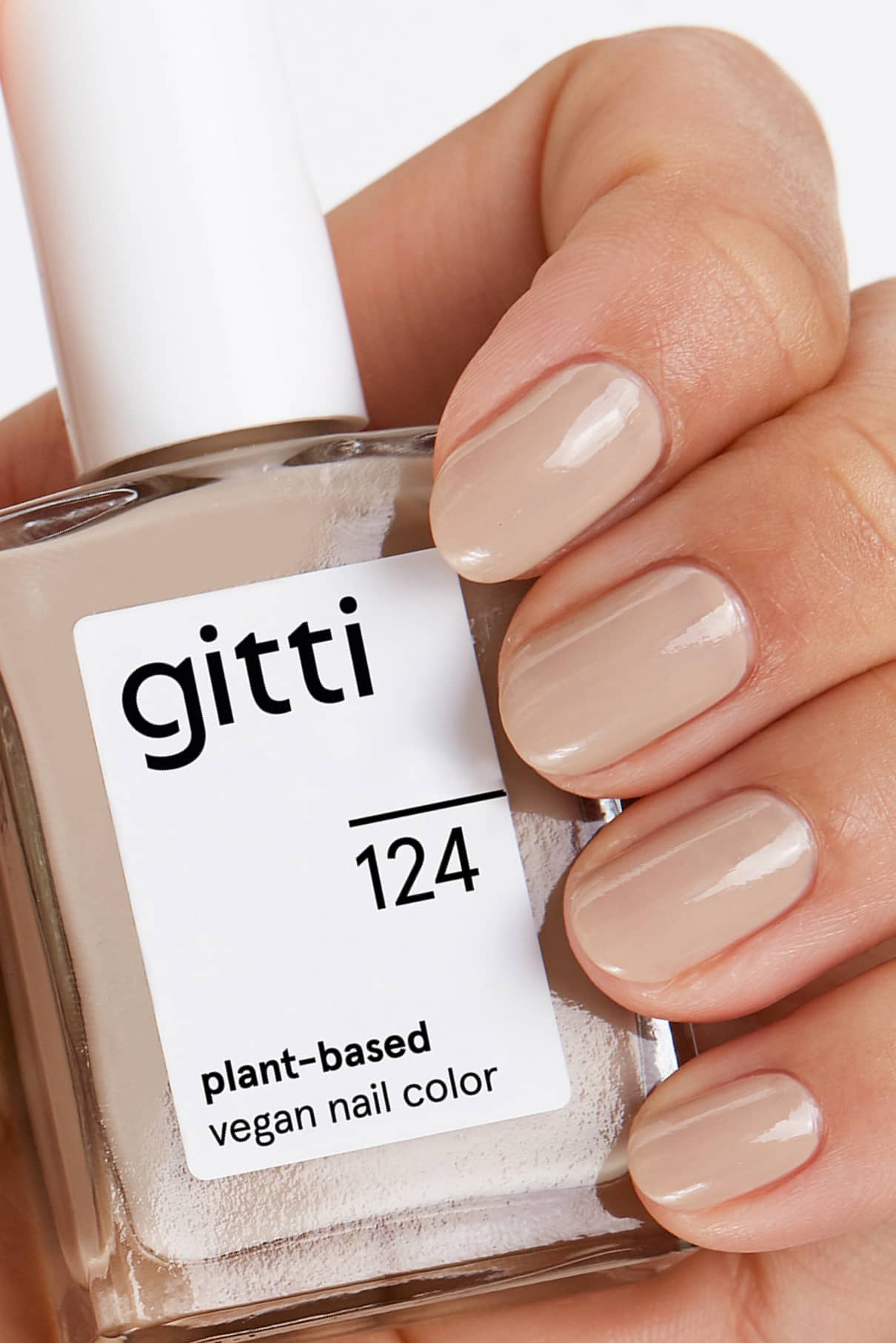 Eine Hand, die eine Flasche gitti no. 124 pflanzliche vegane Nagelfarbe, die Fingernägel sind in einem dezenten Sandton lackiert.