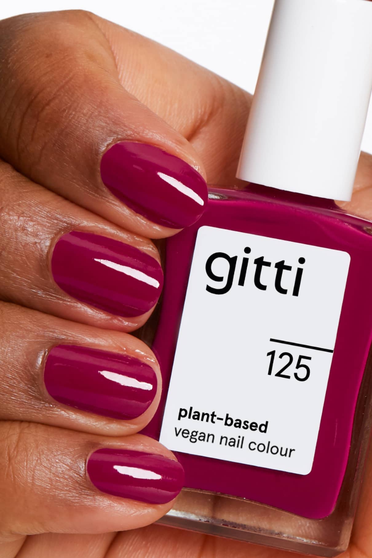 Eine Hand mit sauber manikürten Nägeln, die in einem glänzenden, biervioletten Magentarot-Ton lackiert sind, hält eine Flasche gitti no. 125 vegane Nagelfarbe auf Pflanzenbasis.