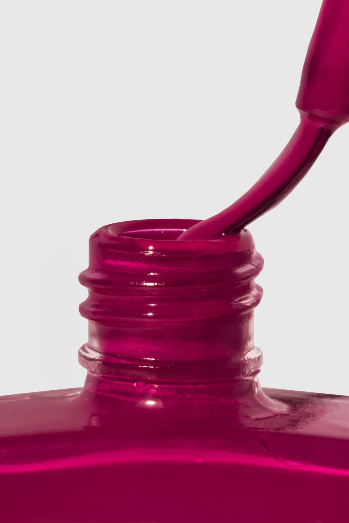 Nahaufnahme eines Nagellackpinsels, der in eine geöffnete Flasche mit Gitti Nr. 125, einem beerenvioletten Magenta-Ton, vor einem schlichten Hintergrund.