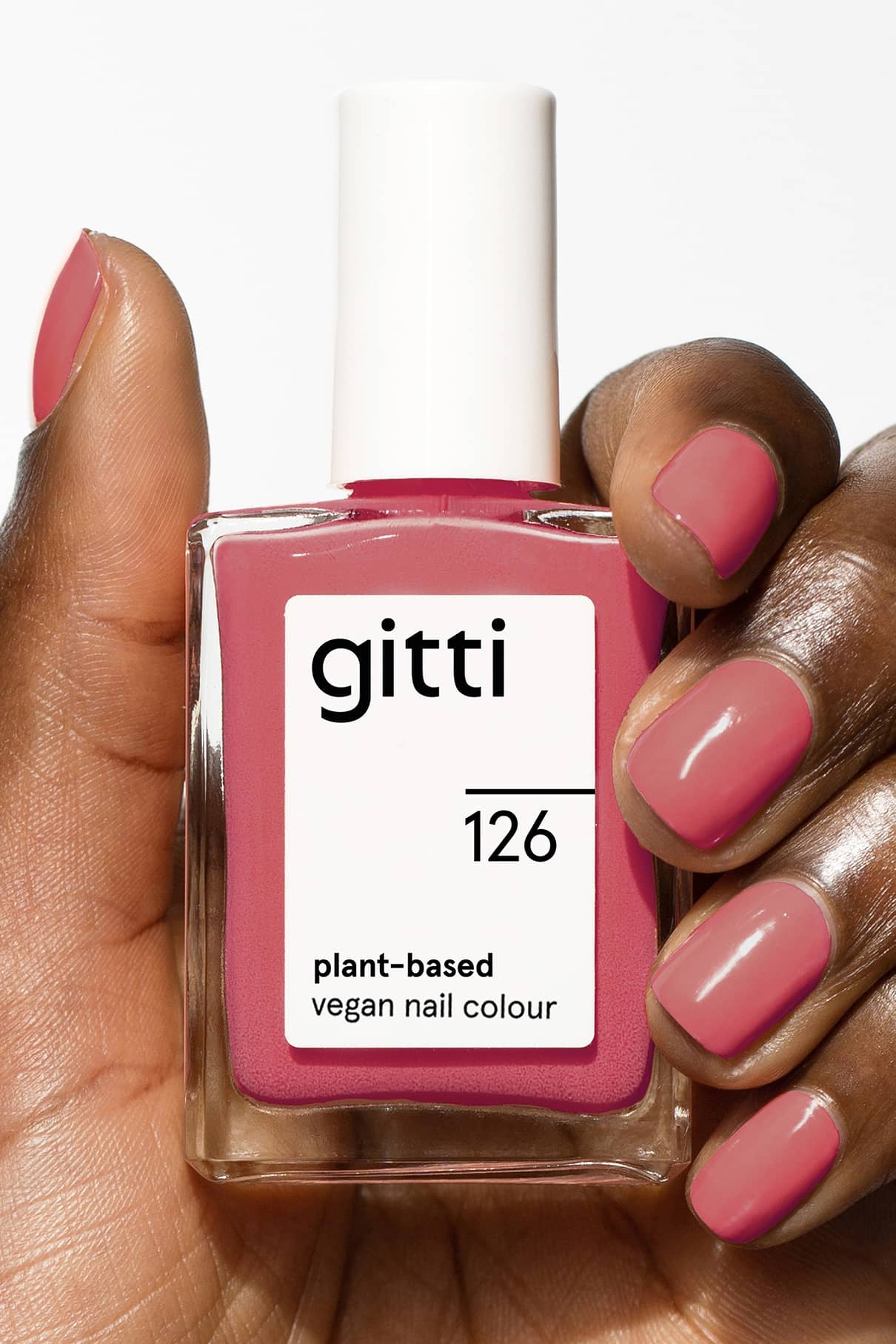 Eine Hand mit polierten Nägeln hält eine Flasche gitti no. 126, einer pflanzlichen, veganen Nagelfarbe in einem pastellfarbenen, sanft-roten Farbton.
