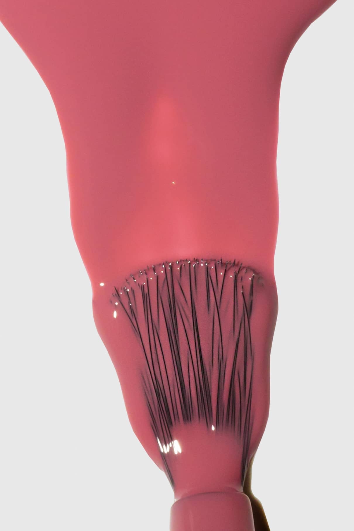 Nahaufnahme eines Pinsels, mit dem glänzender Gitti Nr. 126 Pastellrot-Nagellack, wobei die Borsten durch den nassen Lack auf weißem Hintergrund sichtbar sind.