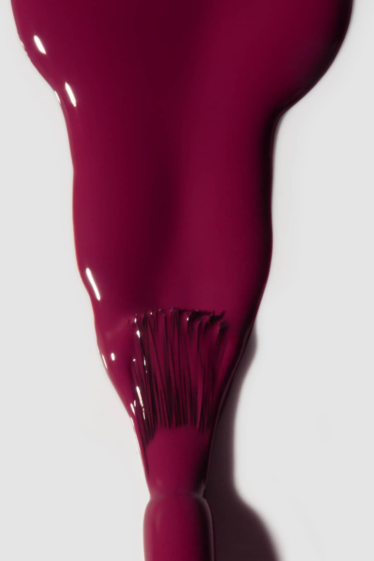 Nahaufnahme eines Pinsels, mit dem eine dicke Schicht von gitti no. 127 Nagellack in der Farbe berry plum auf eine weiße Fläche auf.
