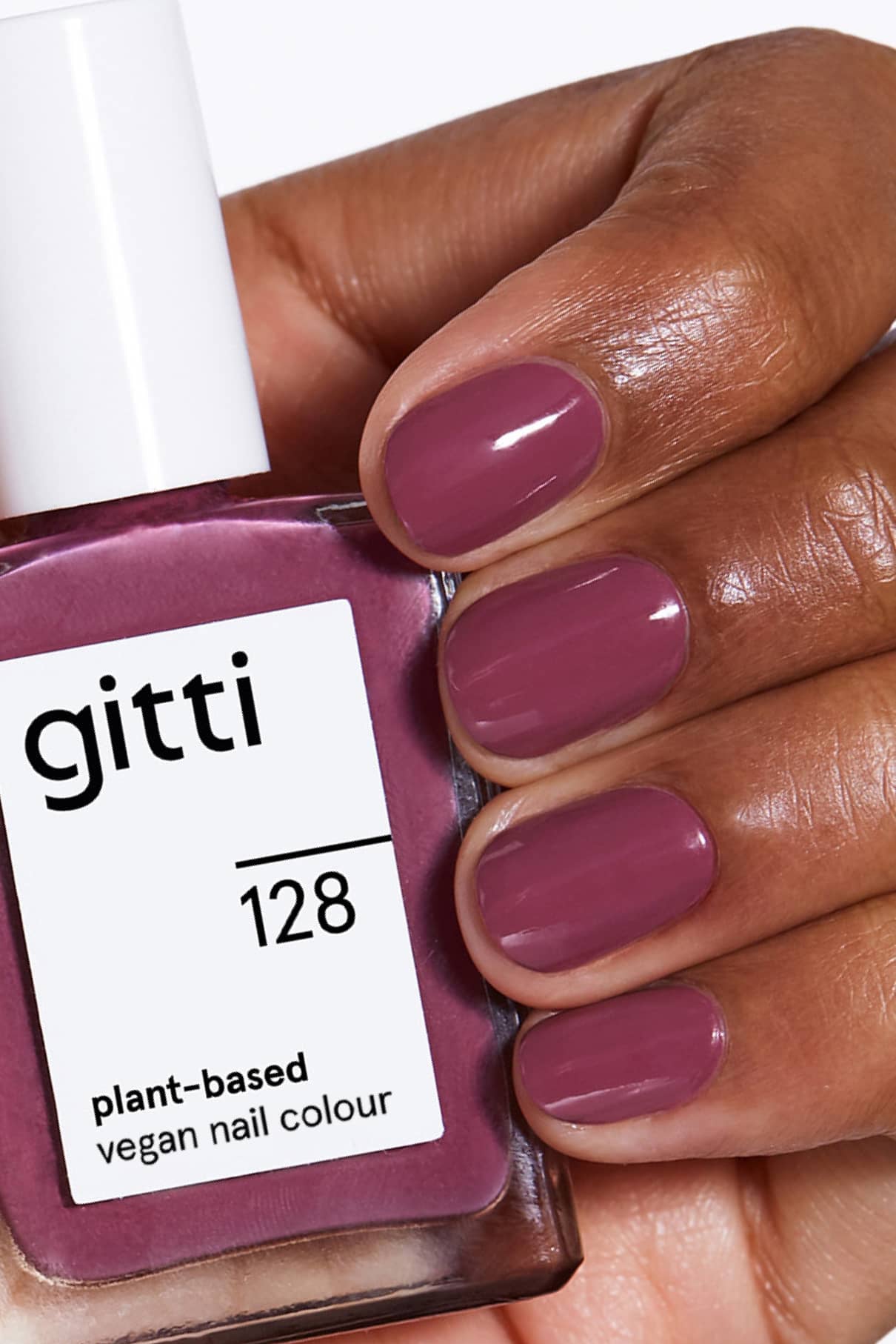 Eine Hand mit sauber manikürten, in dunklem Lila lackierten Nägeln hält eine Flasche mit gitti no. 128, eine vegane Nagelfarbe auf Pflanzenbasis, die perfekt zum Lack passt.