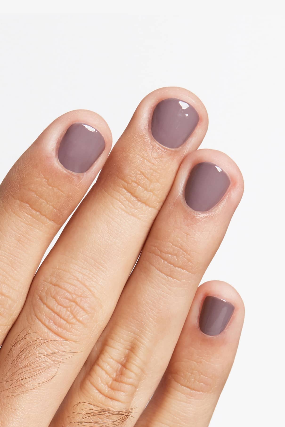 Eine Hand mit kurzen, sauber gefeilten Nägeln, lackiert in glänzendem gitti no. 129 Grau-Violett taupe vor einem weißen Hintergrund für einen eleganten, modernen Look.