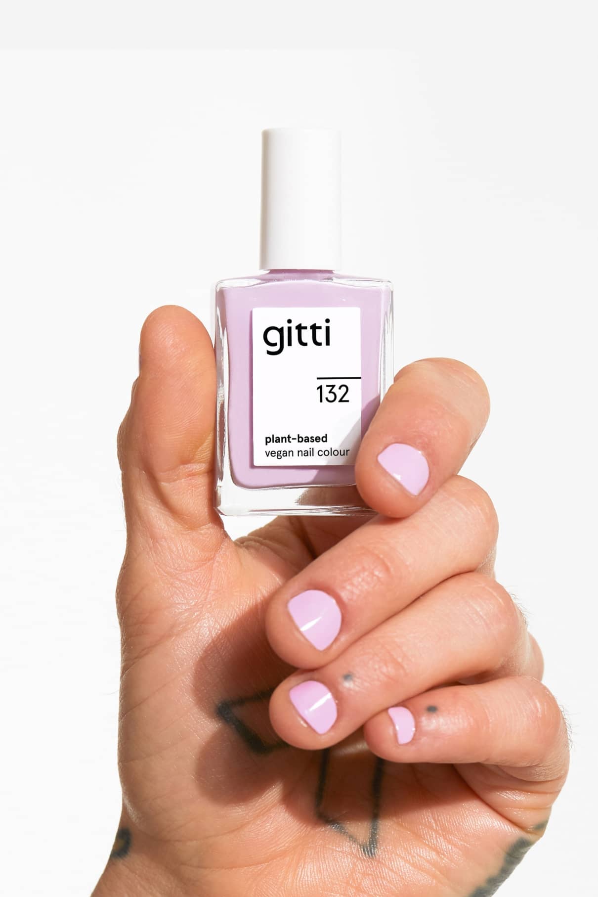 Eine Hand mit pastelllila Nägeln hält eine Flasche gitti no. 132 vegane Nagelfarbe auf Pflanzenbasis.