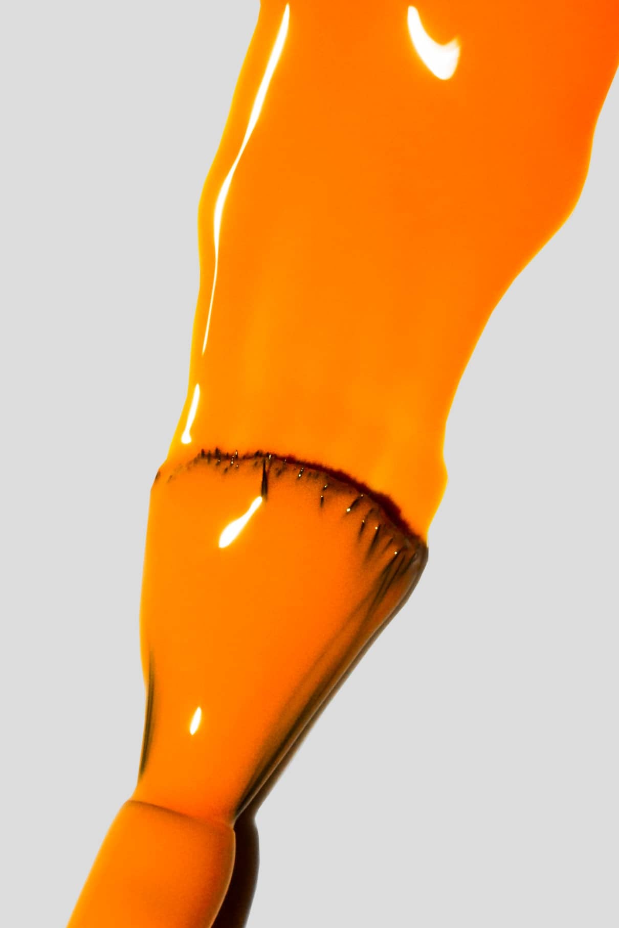 Nahaufnahme eines Pinsels mit Gitti Nr. 133, einem leuchtenden Orangeton, auf den Borsten vor einem schlichten hellgrauen Hintergrund.