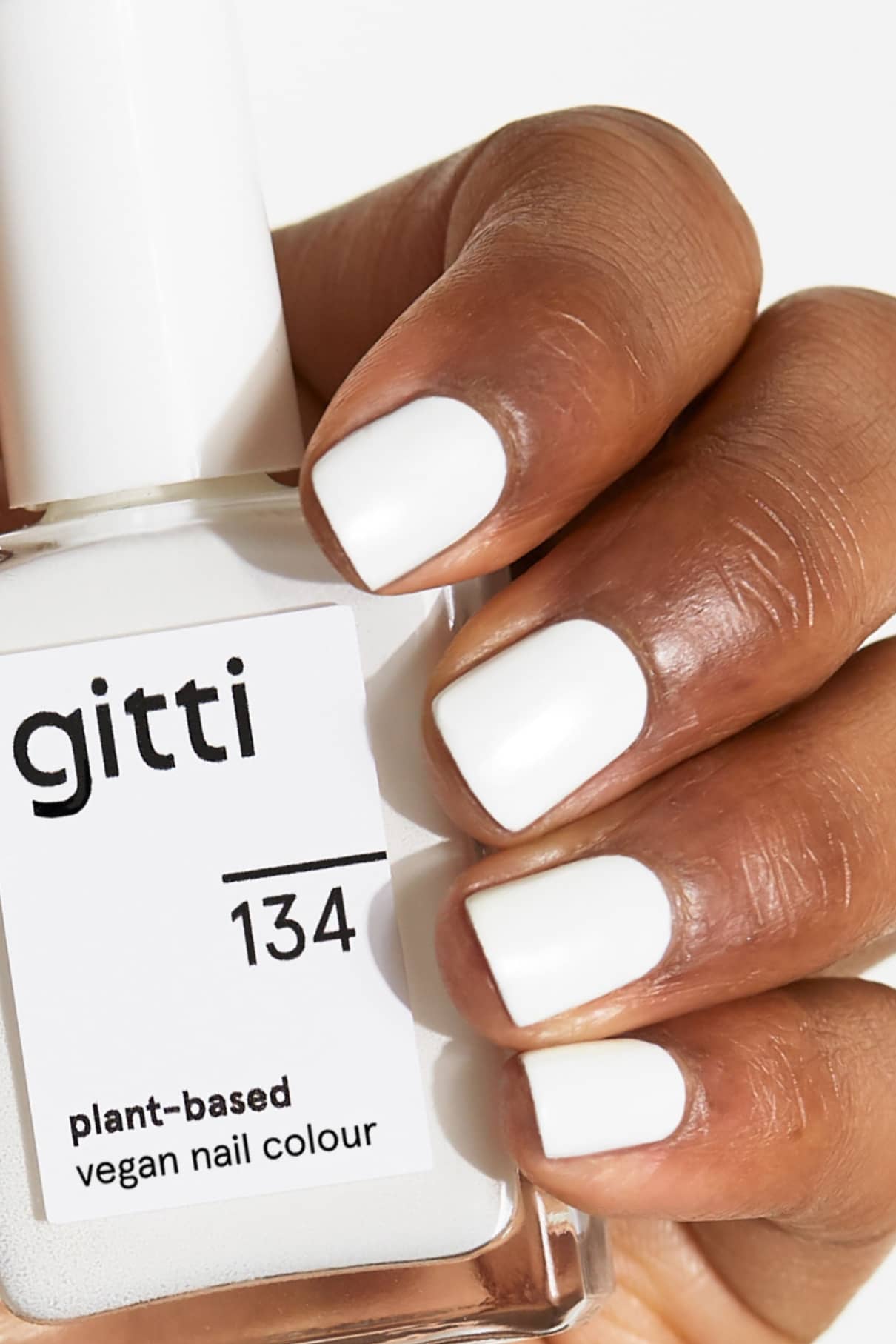 Eine Hand mit sauber manikürten, in minimalistischem Weiß lackierten Nägeln hält ein Fläschchen mit gitti no. 134 pflanzlicher, veganer Nagellack.