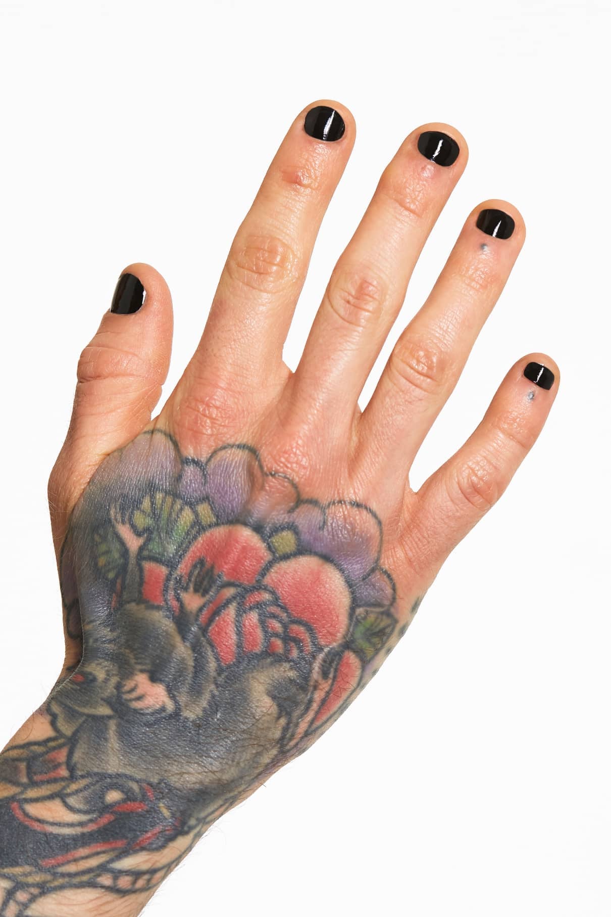 Eine Hand mit gitti no. 135 tief-leuchtendes Schwarz Nagellack und bunten Tattoos, die eine detaillierte Ratte, Blumen und Blätter auf dem Handrücken zeigen.