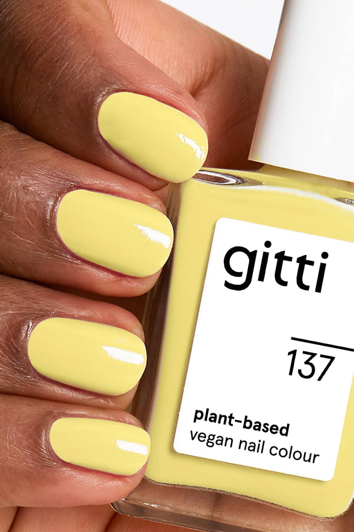 Nahaufnahme einer Hand mit gelb lackierten Nägeln, die eine Flasche gitti no. 137, einem veganen Nagellack auf Pflanzenbasis in leuchtendem Gelb.