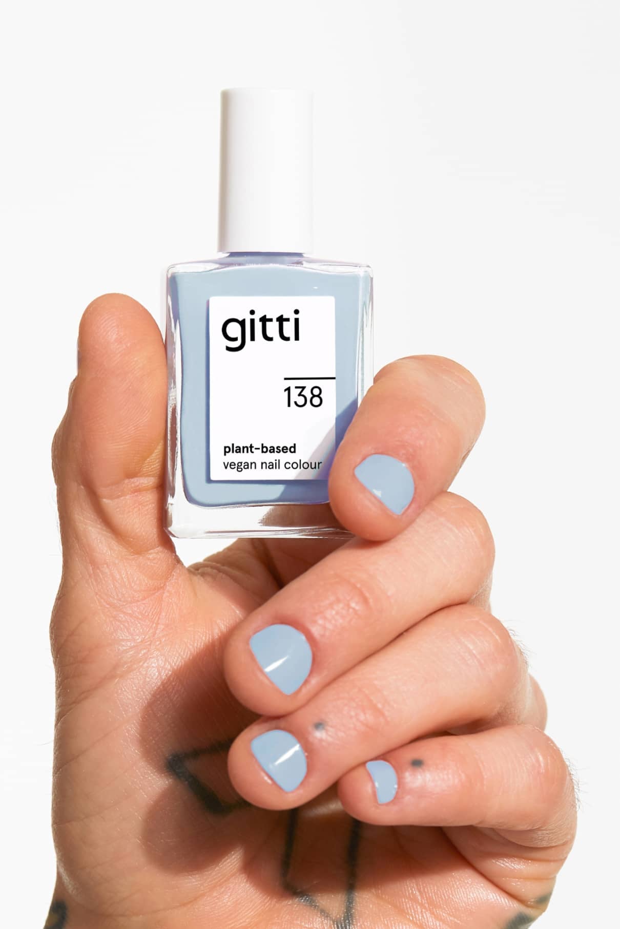Eine Hand mit blau lackierten Nägeln hält eine Flasche von gitti no. 138, einem pflanzlichen, veganen Nagellack in einem kühlen Denim-Blau.