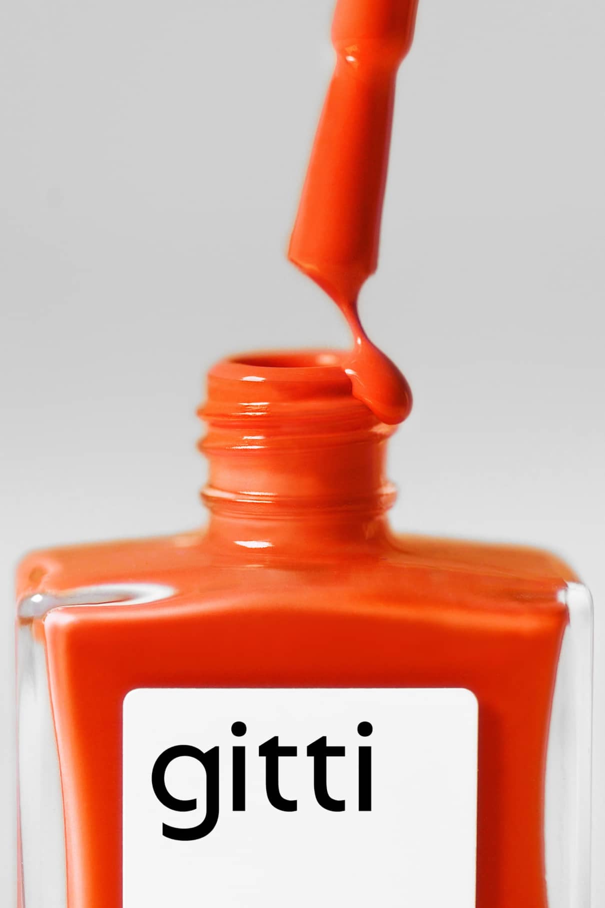 Eine geöffnete Flasche gitti no. 139 Nagellack, dessen Pinsel leuchtendes Orangerot tropft, hebt sich von einem schlichten Hintergrund ab.