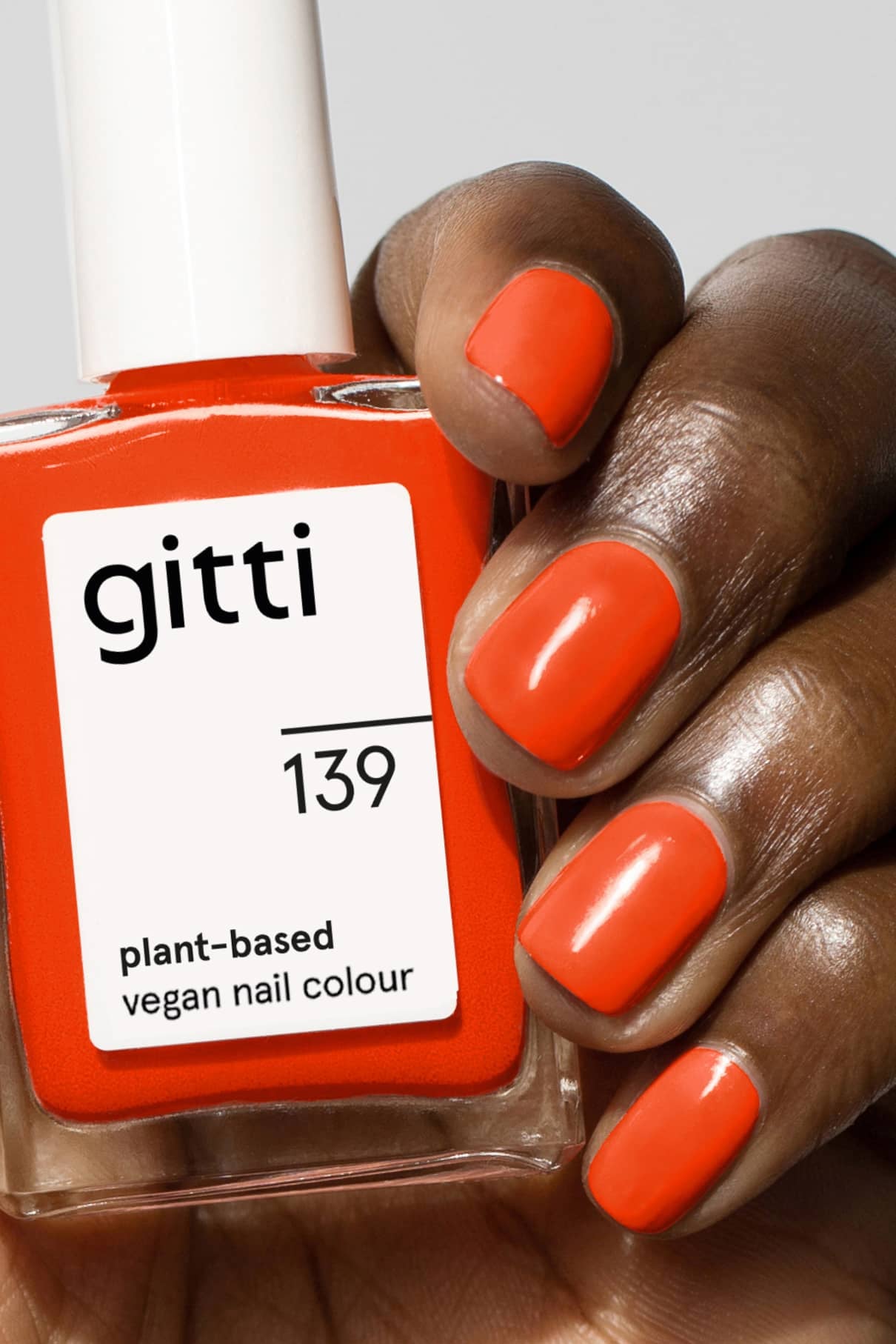 Eine Hand mit orange lackierten Nägeln hält eine Flasche gitti no. 139 pflanzliche vegane Nagelfarbe in intensivem Orangerot, die perfekt zu dem leuchtenden Farbton passt.
