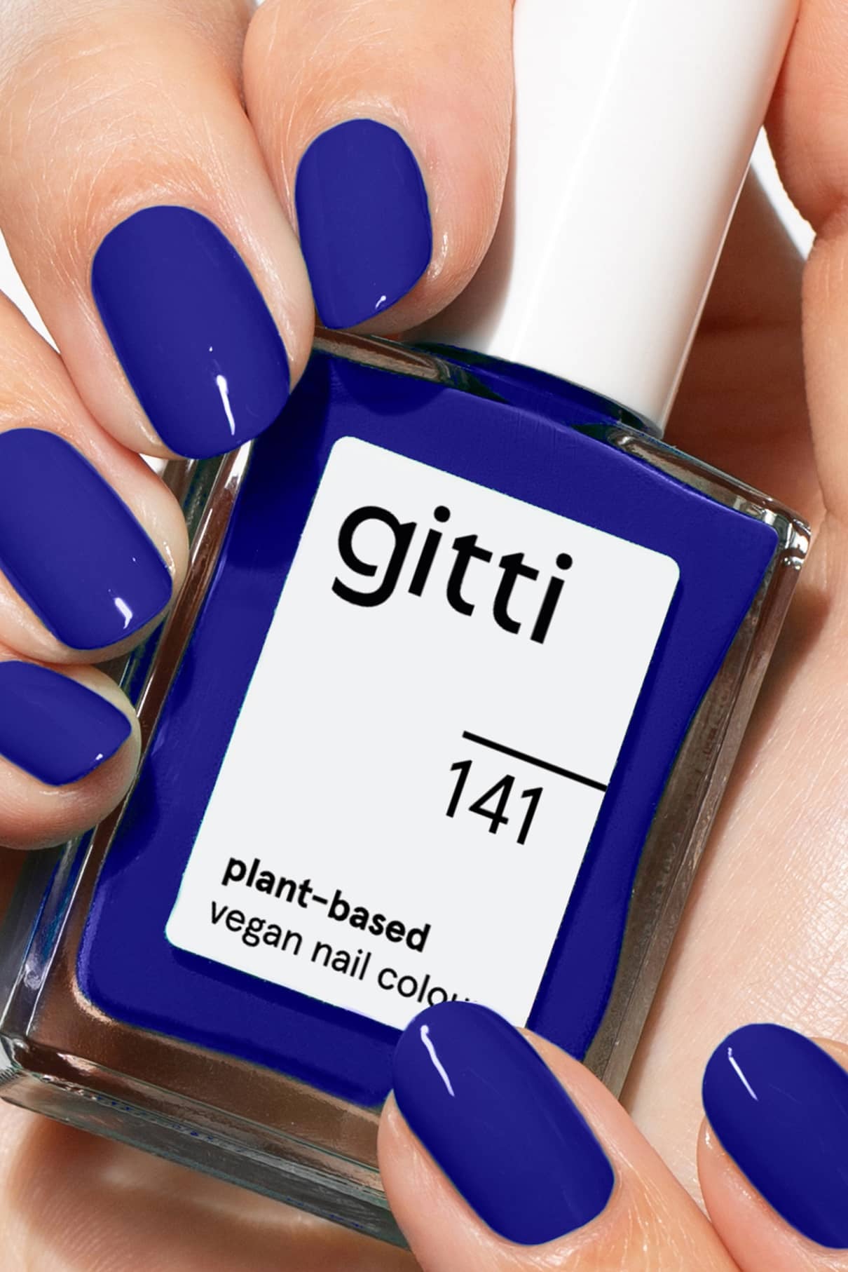 Nahaufnahme von Händen mit intensiv blau lackierten Nägeln, die eine Flasche gitti no. 141, einem veganen Nagellack auf Pflanzenbasis.