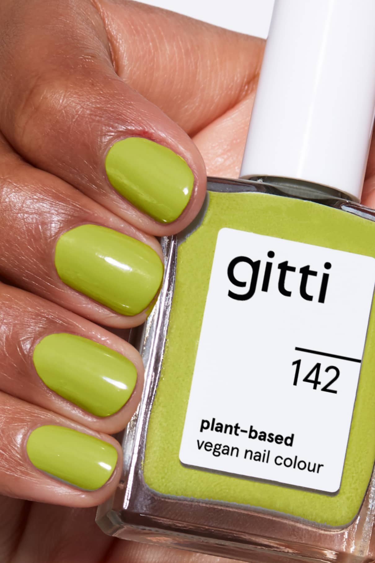 Eine Hand mit kurzen, sauber lackierten gelbgrünen Nägeln hält ein Fläschchen mit gitti no. 142 pflanzlicher, veganer Nagelfarbe im gleichen frischen Farbton.