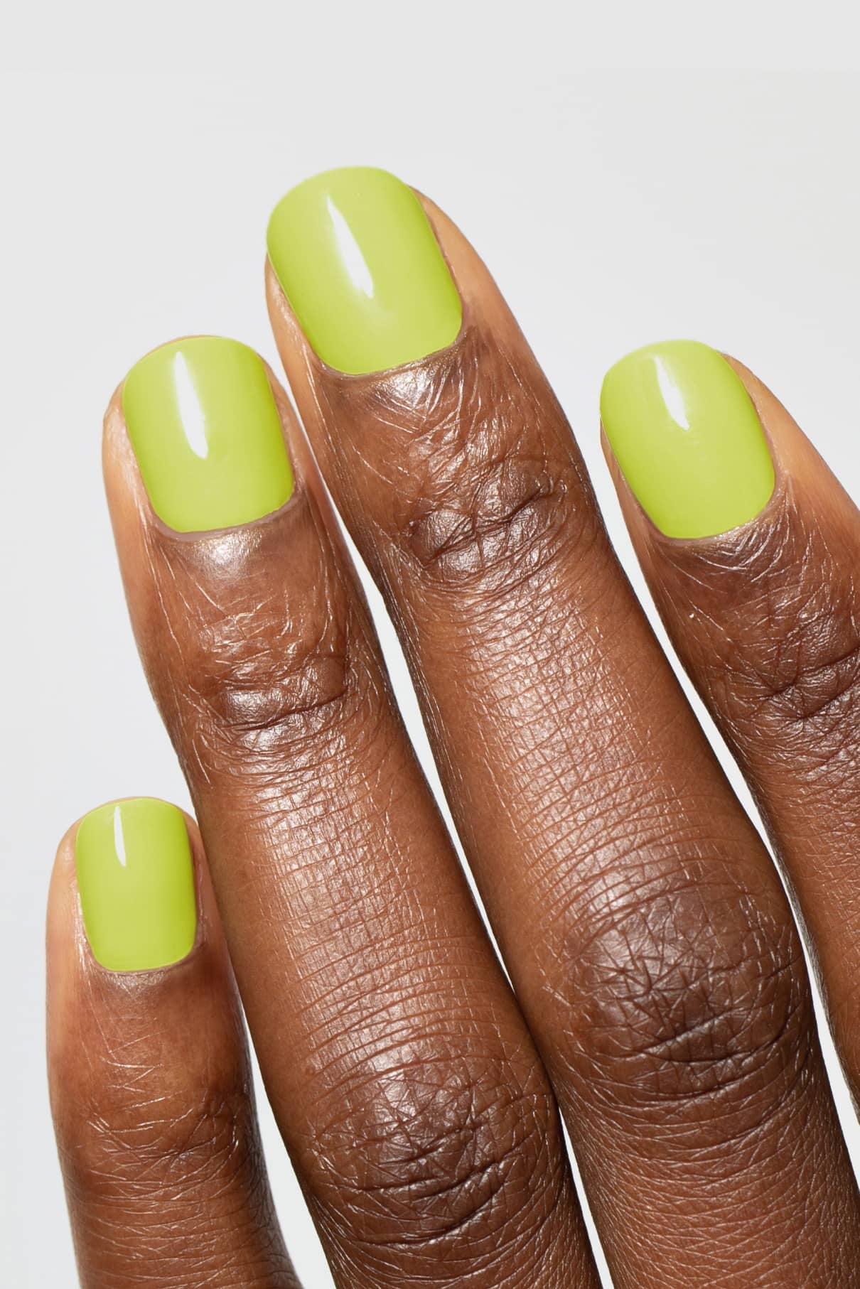 Nahaufnahme einer Hand mit kurzen, quadratisch geformten Fingernägeln, die mit glänzendem gitti no. 142, einem frischen gelbgrünen Nagellack.