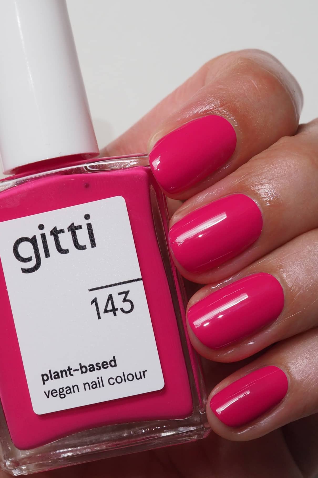 Eine Hand mit kurzen, leuchtend rosa lackierten Nägeln hält eine Flasche gitti no. 143 pflanzlichen veganen Nagellack, der perfekt zur leuchtenden Nagelfarbe passt.