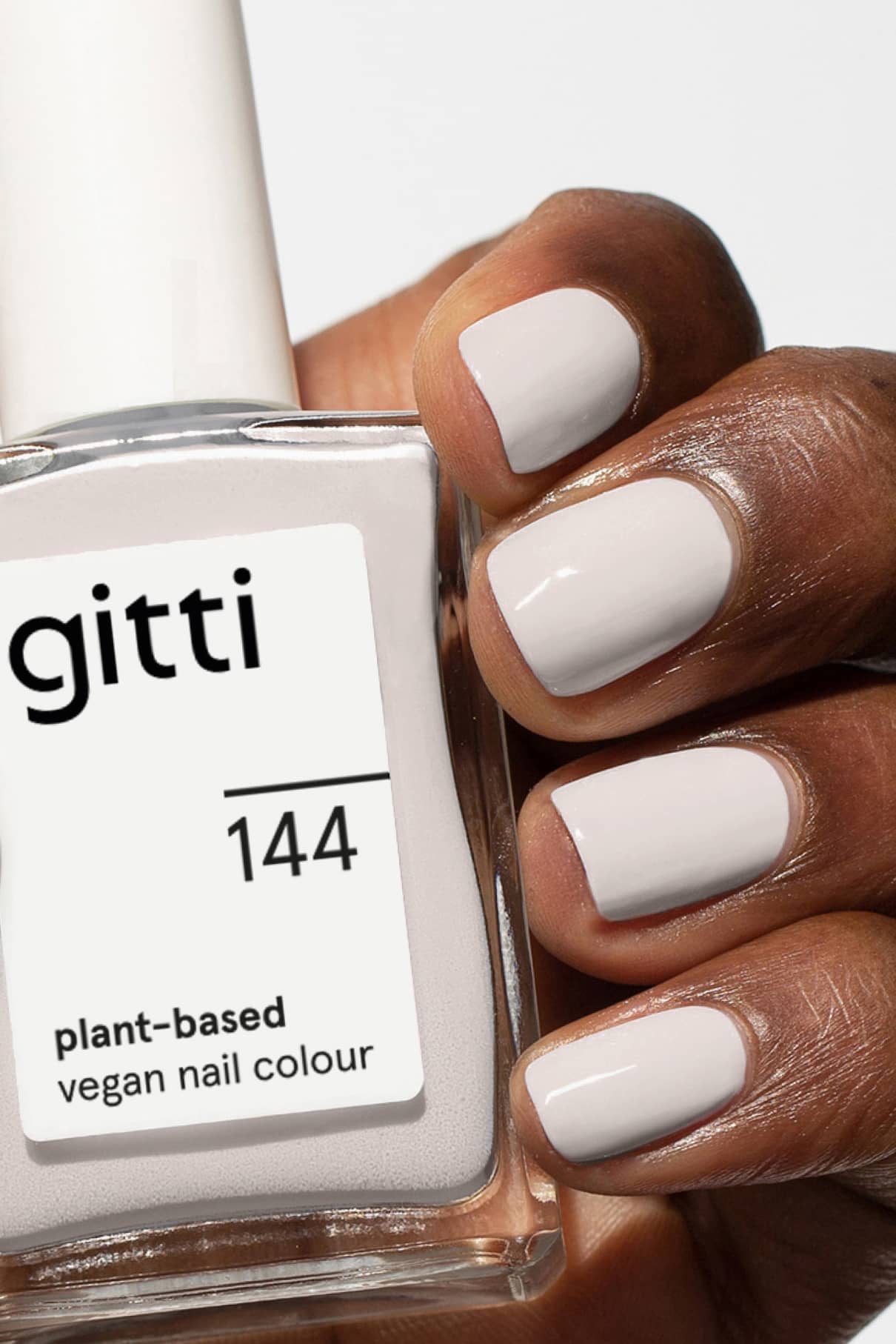 Eine Hand mit hellbeigem Nagellack hält eine Flasche mit der Aufschrift gitti no. 144, eine vegane Nagelfarbe auf Pflanzenbasis in zeitlosem Grau.