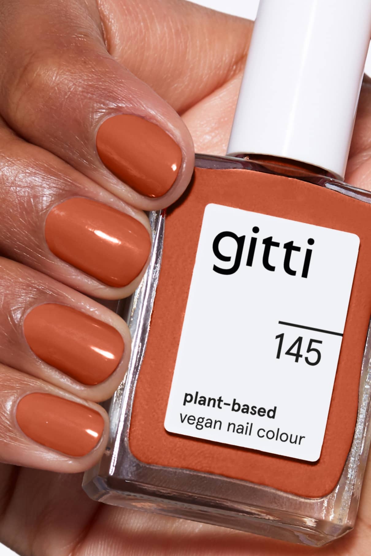 Eine Hand mit sauber manikürten, in einem Zimtbraun-Ton lackierten Nägeln hält eine Flasche gitti no. 145, einem pflanzlichen, veganen Nagellack in der passenden Farbe Warmes Braun.