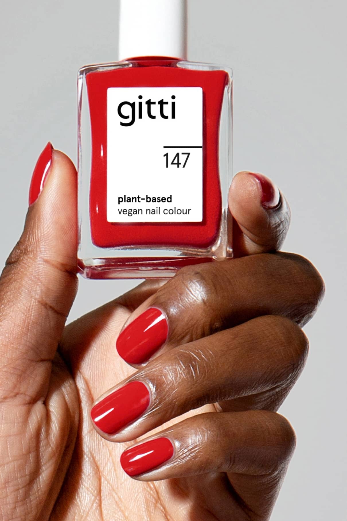 Eine Hand mit sauber manikürten, klassisch roten Nägeln hält eine Flasche gitti no. 147 vegane Nagelfarbe auf Pflanzenbasis.