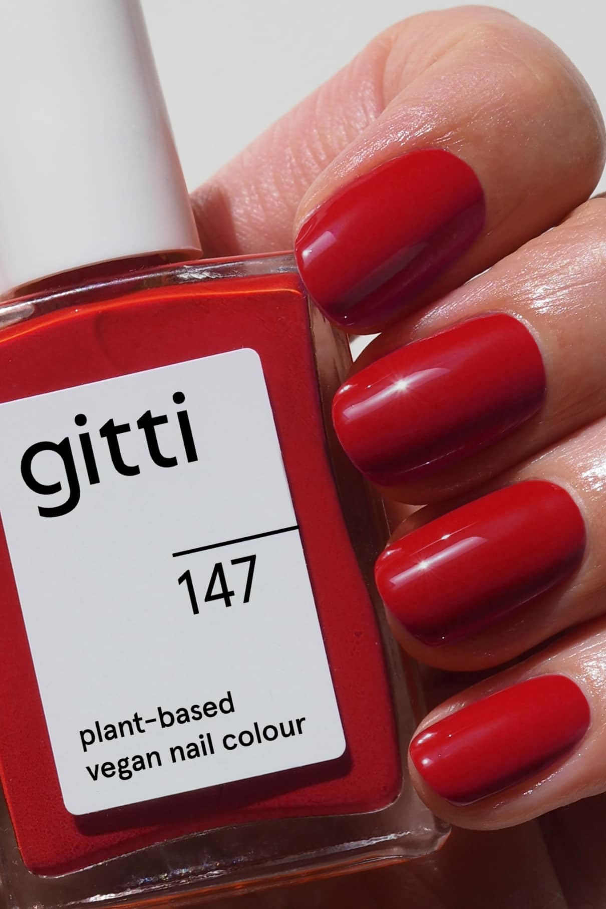 Eine Hand mit sauber manikürten roten Nägeln hält eine Flasche gitti no. 147 veganen Nagellack auf Pflanzenbasis in klassischem Rot.