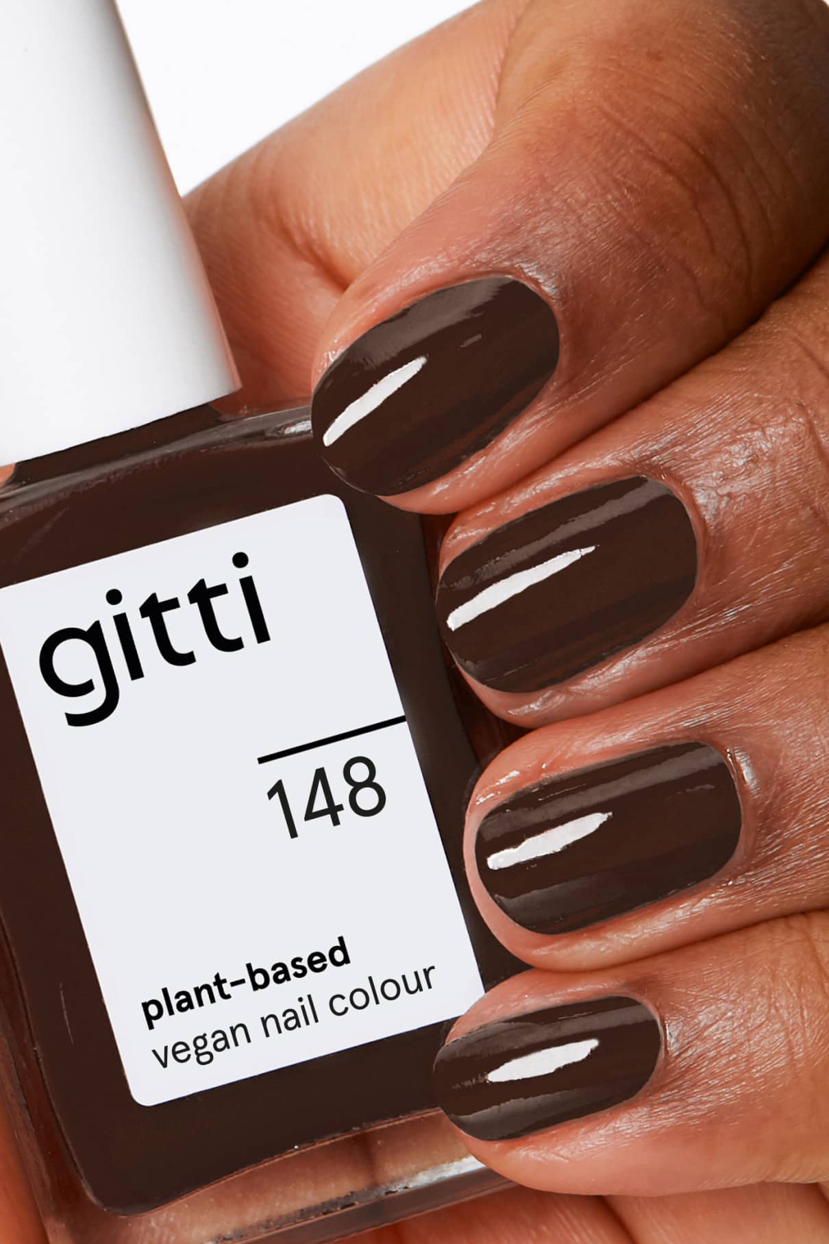 Eine Hand mit sauber manikürten Nägeln, die mit gitti no. 148, einer veganen Nagelfarbe auf Pflanzenbasis in einem intensiven Braunton, hält eine Flasche mit der Aufschrift gitti no. 148.